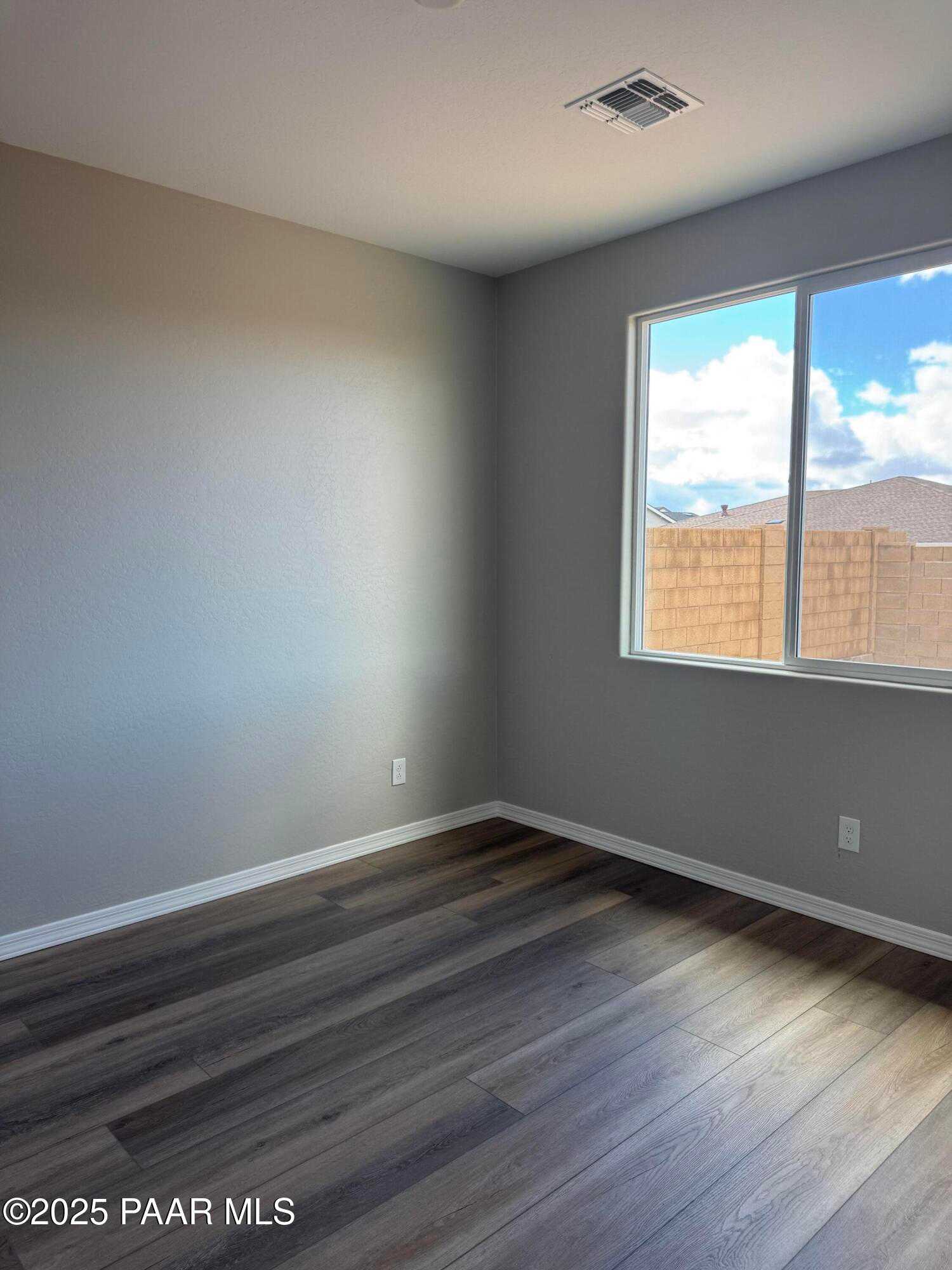 Bright empty room with gray walls, luxury vinyl plank wood flooring, and large window overlooking Prescott, AZ neighborhood in The Monarch A home