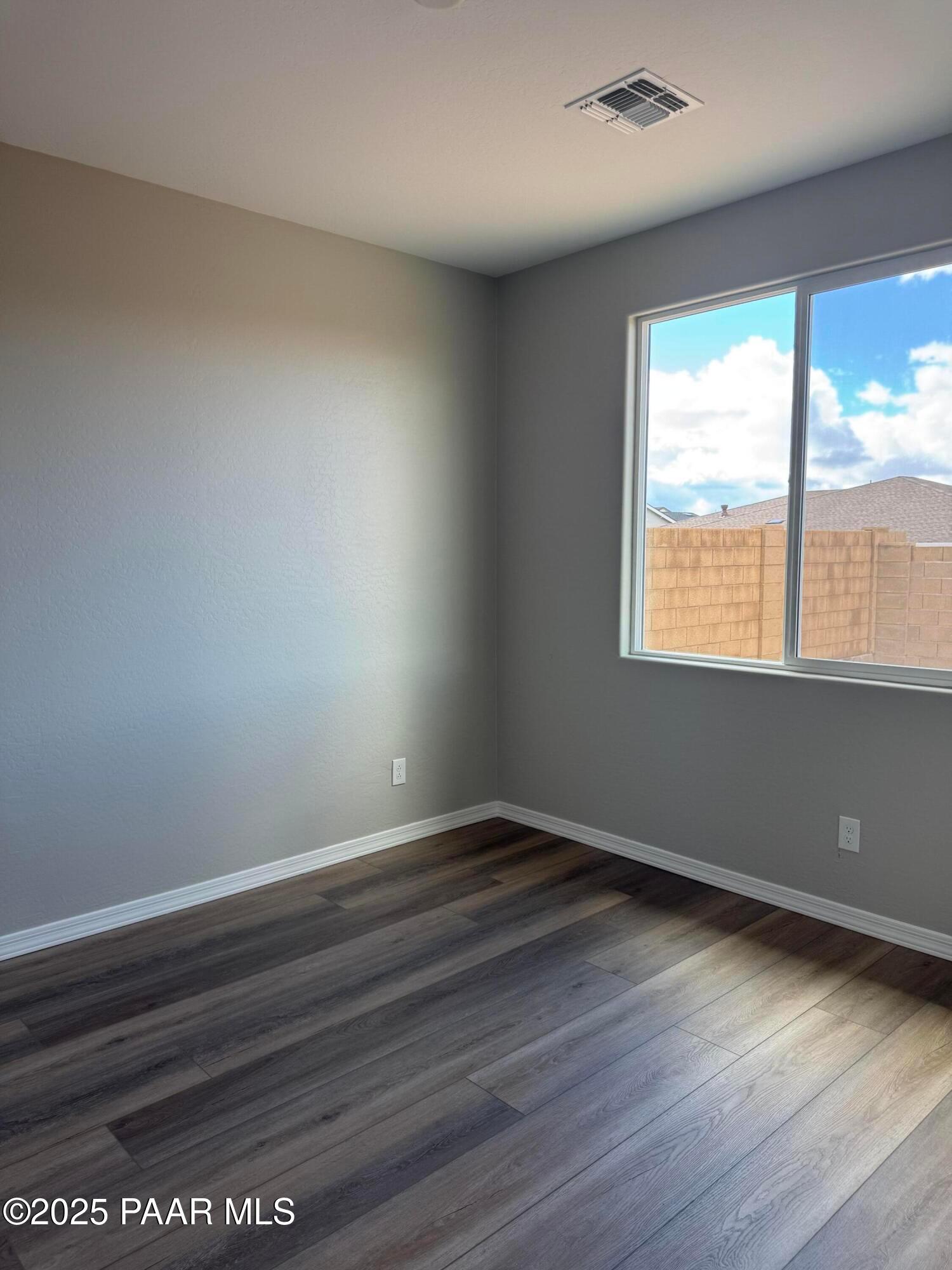 Bright empty room with gray walls, luxury vinyl plank wood flooring, and large window overlooking Prescott, AZ neighborhood in The Monarch A home