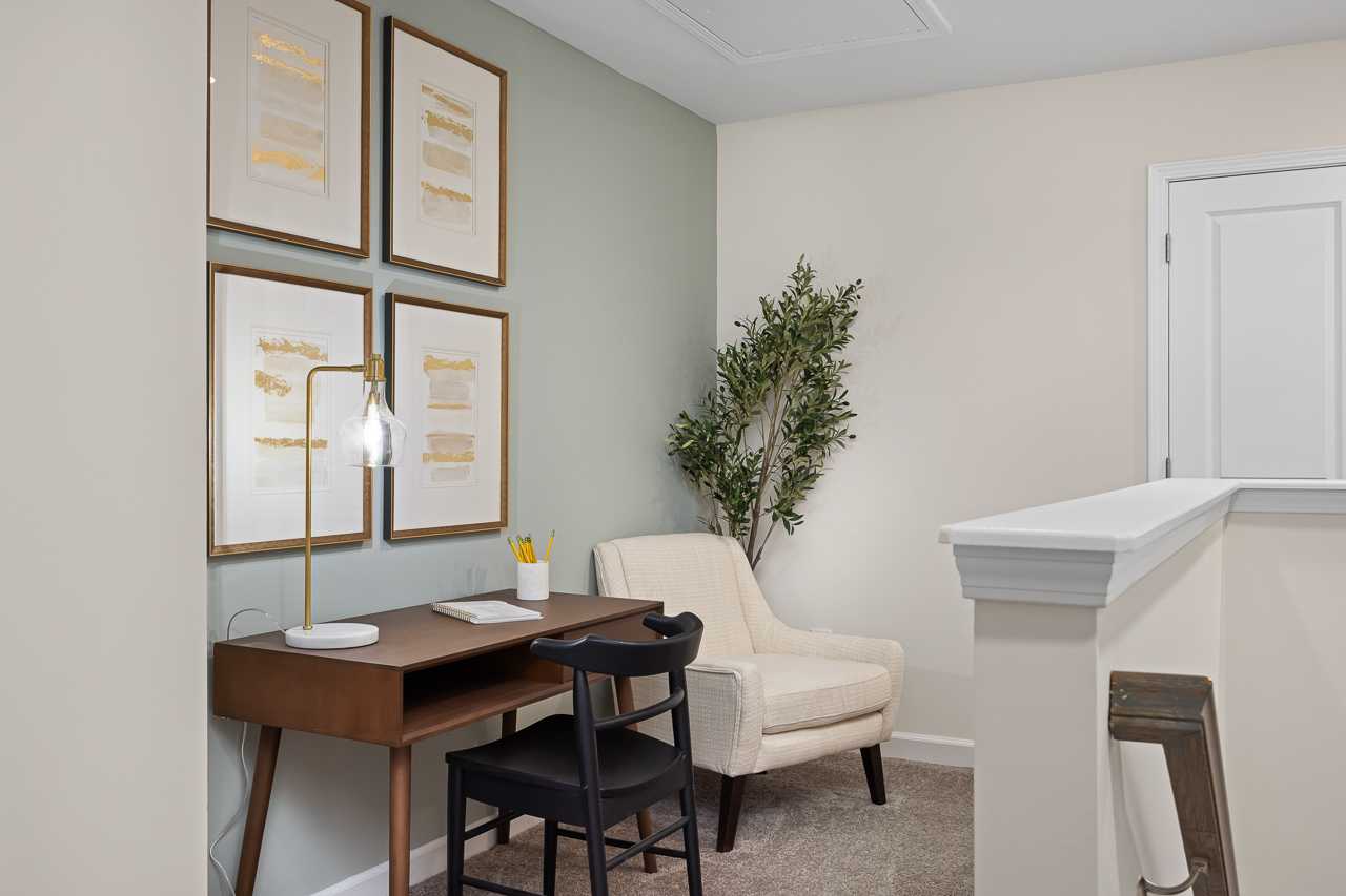 Cozy home office with wooden desk, armchair, gold lamp, abstract art, and potted plant at Gregory Village Townhomes in Lillington NC