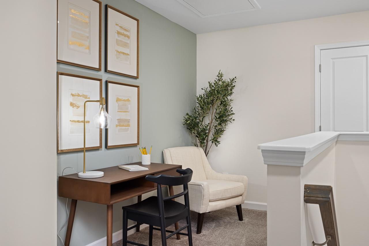 Cozy home office with wooden desk, armchair, gold lamp, abstract art, and potted plant at Gregory Village Townhomes in Lillington NC