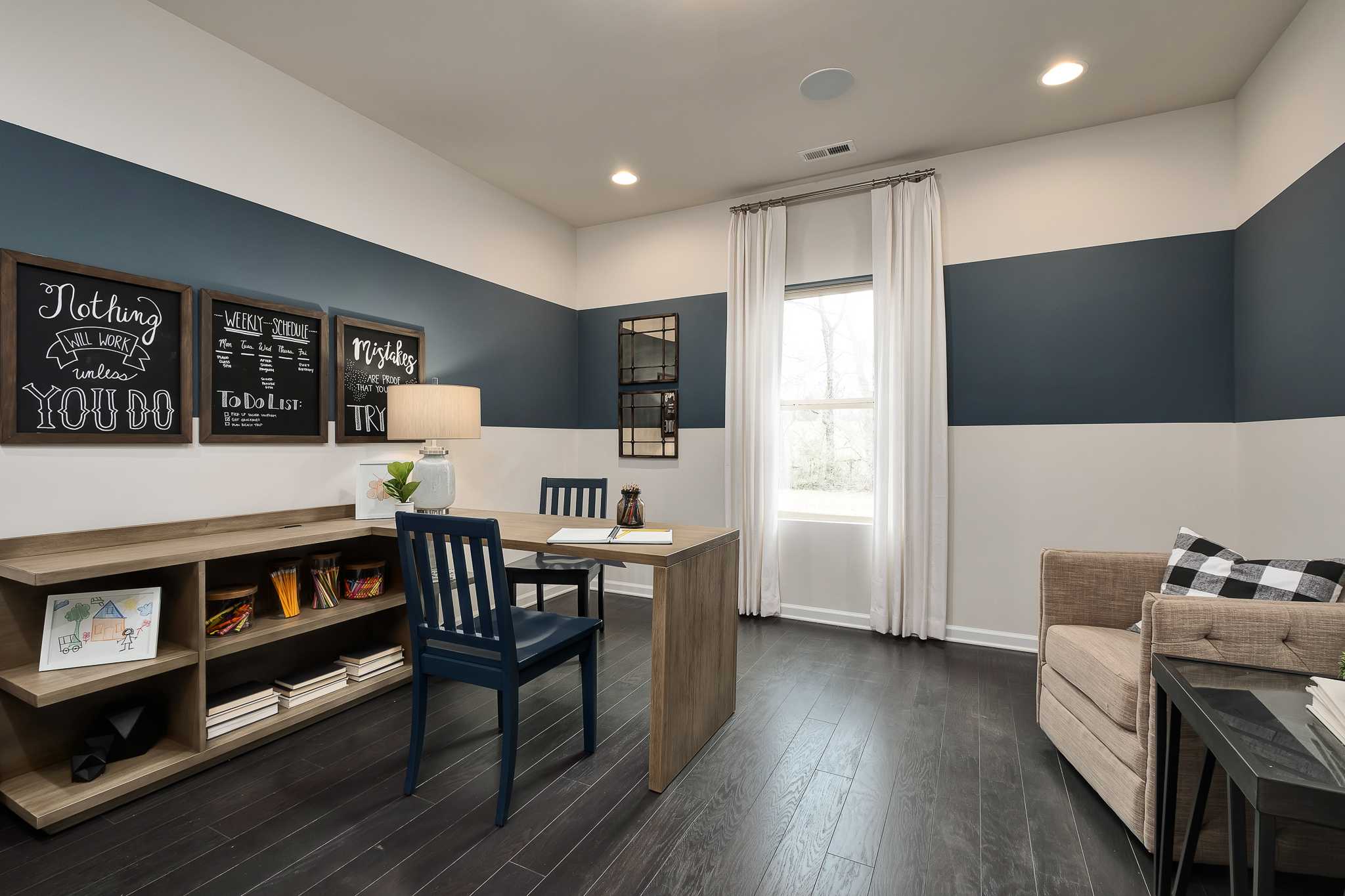 Modern home office at The Reserve at Overton in Hampton Cove, Alabama featuring navy accent wall, wooden desk, and bookshelves