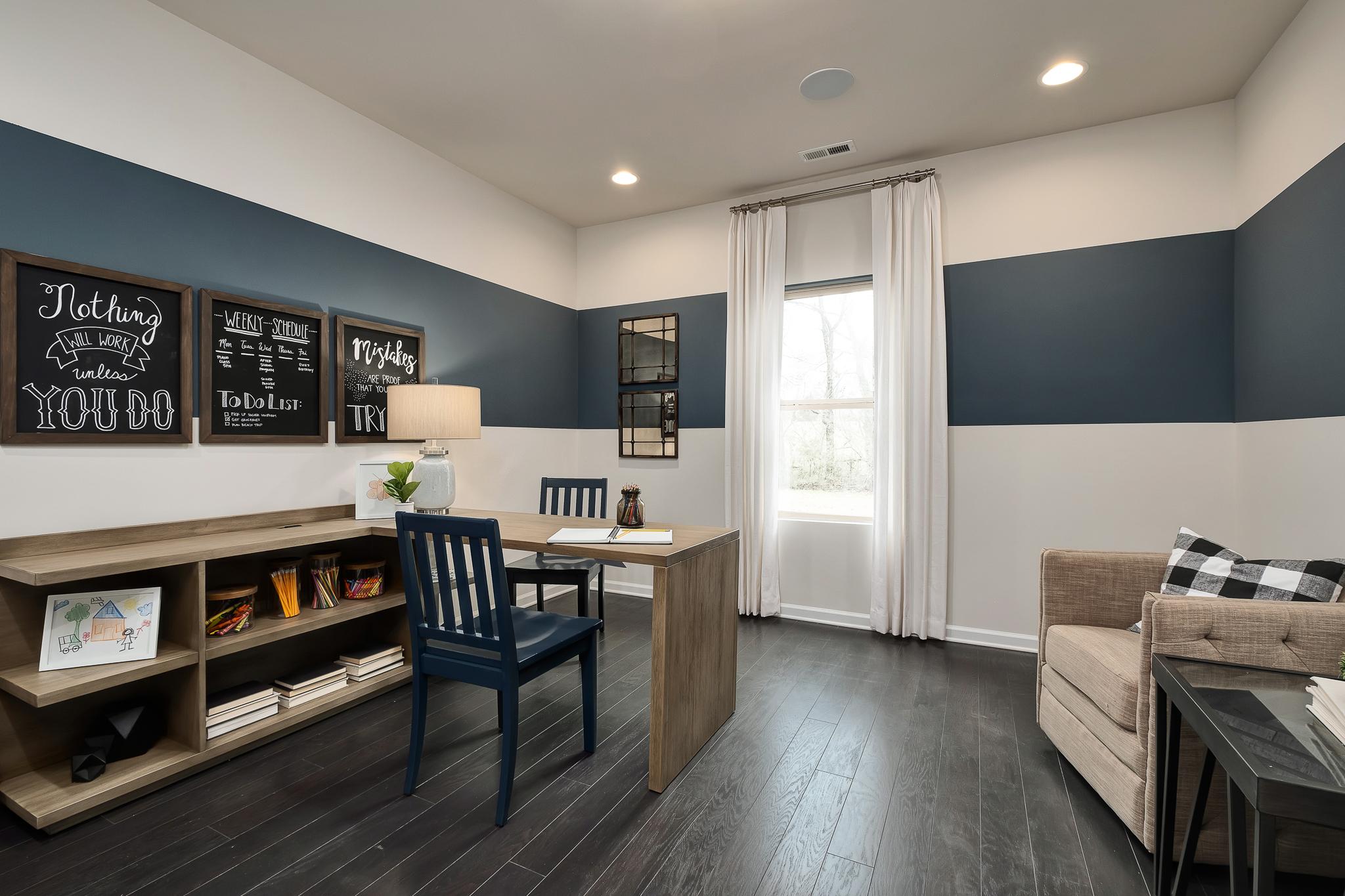 Modern home office at The Reserve at Overton in Hampton Cove, Alabama featuring navy accent wall, wooden desk, and bookshelves