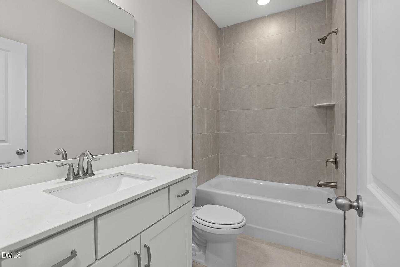 Modern guest bathroom with white quartz vanity, soaking tub, separate shower, and neutral tile in Davidson Homes The Beech C, Wake Forest