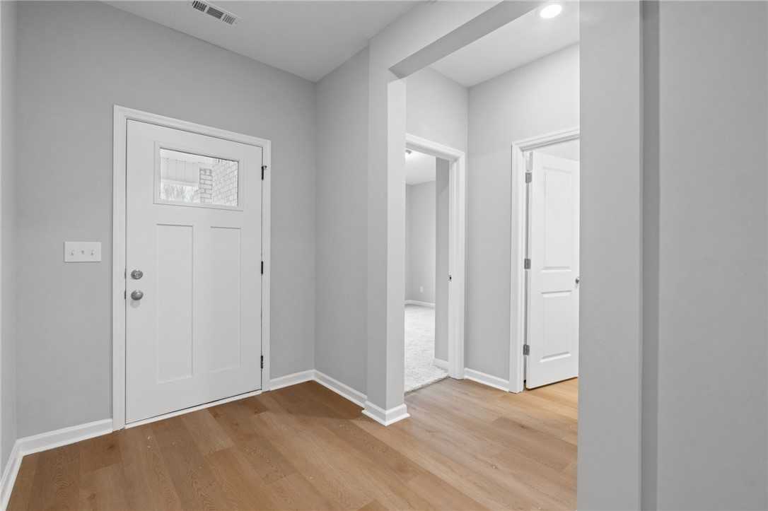 Bright entryway with white glass-panel door, archway, and oak hardwood floors in Davidson Homes The Luna B, Opelika