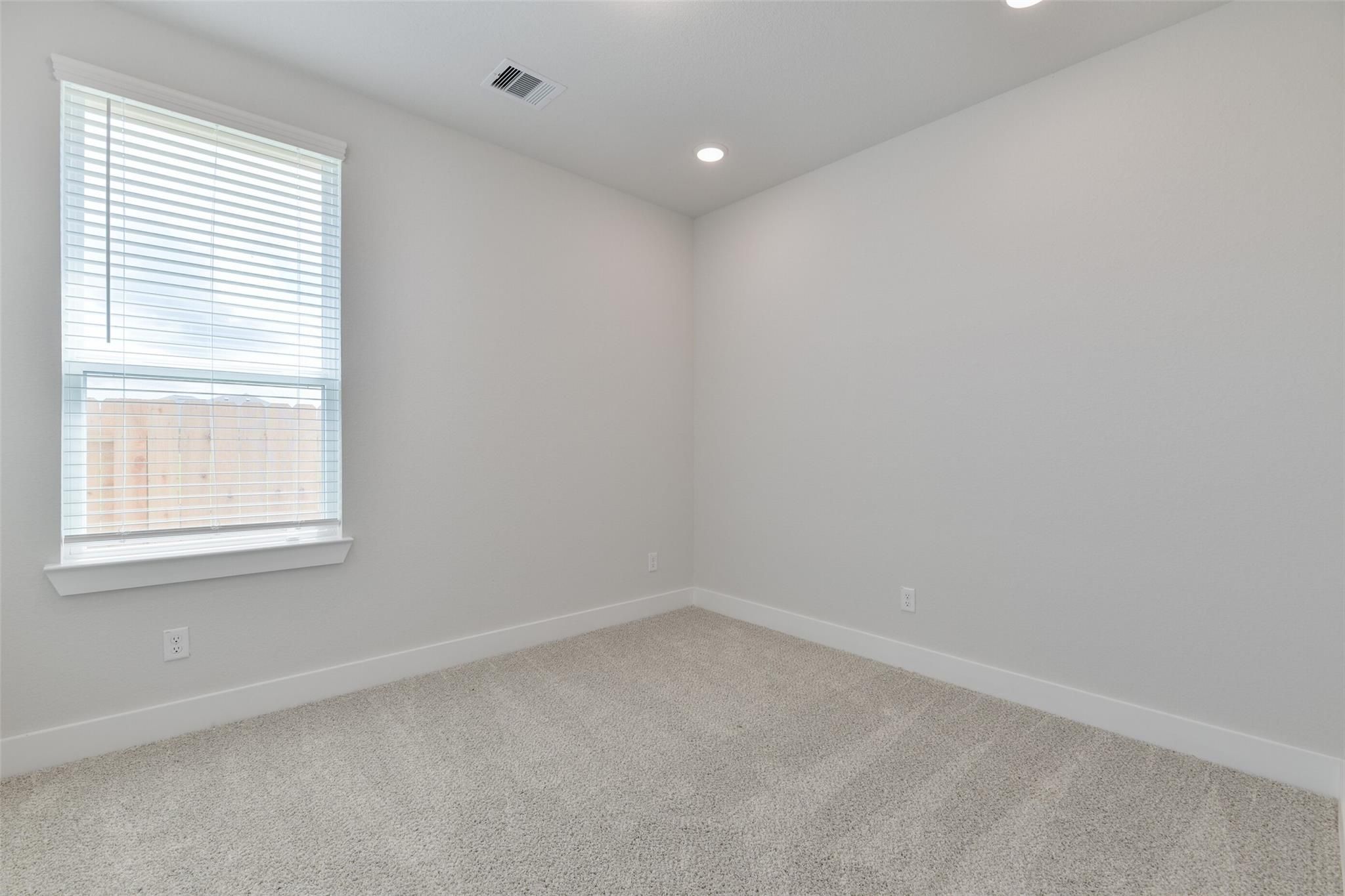 Bright secondary bedroom with light gray walls, carpet flooring, and window blinds in Davidson Homes The Edward A, Lago Mar, Texas