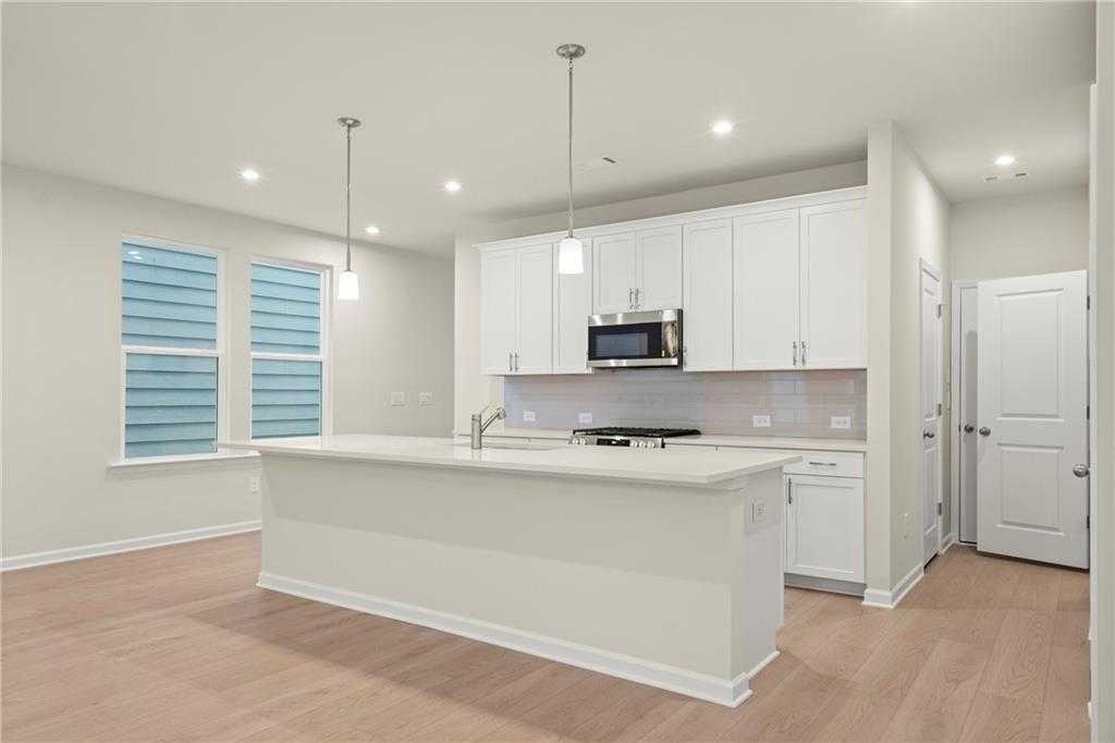 Modern open-concept kitchen with white island, stainless microwave, pendant lights in The Cary A Davidson Homes, Kennesaw, GA