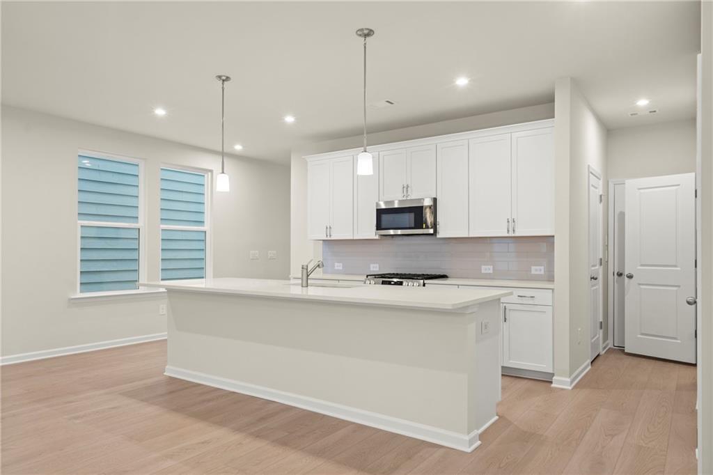 Modern open-concept kitchen with white island, stainless microwave, glass backsplash in Davidson Homes The Cary A, Kennesaw, GA