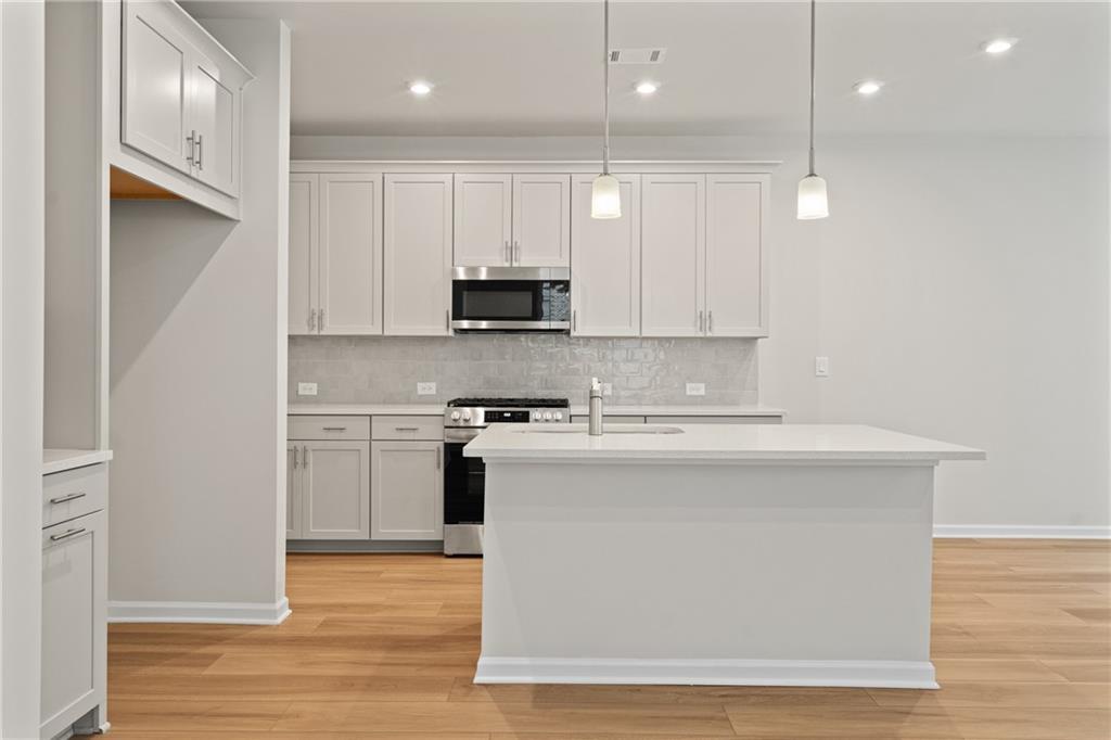Modern white kitchen featuring large island, stainless steel appliances, subway tile backsplash in Davidson Homes The Marion B, Kennesaw, GA