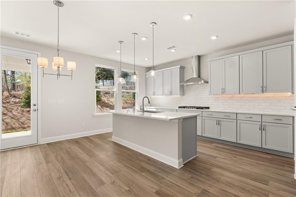 Bright modern kitchen with white quartz island, gray shaker cabinets, subway tile backsplash in The Danbury C, Buford, GA