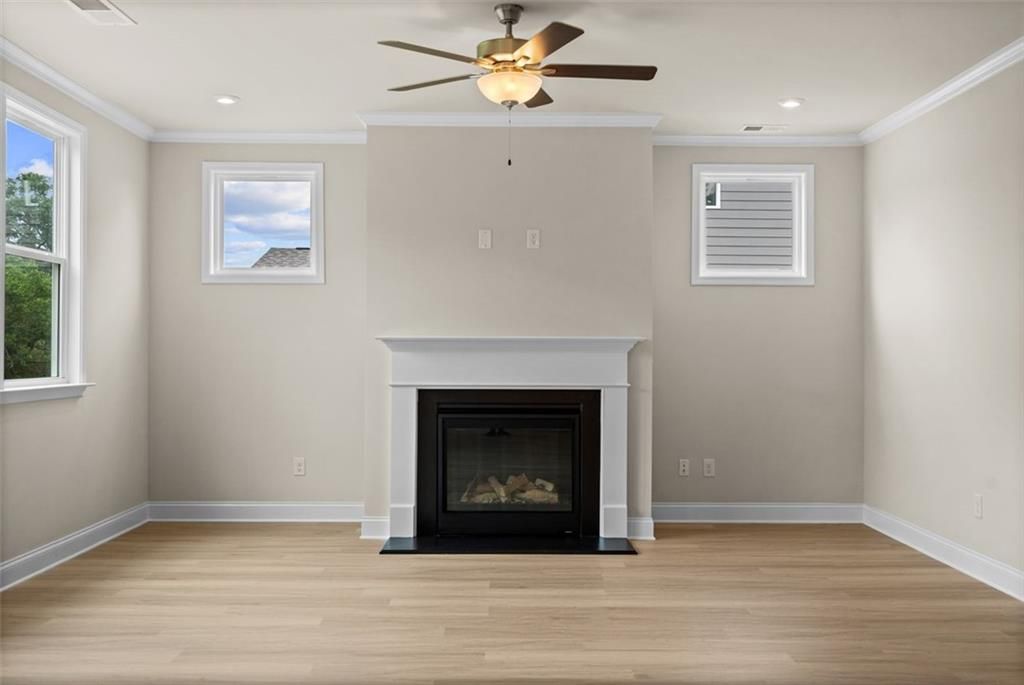 Cozy family room featuring gas fireplace, ceiling fan, hardwood floors, and large windows in Davidson Homes The Hickory B at Wehunt Meadows, Hoschton