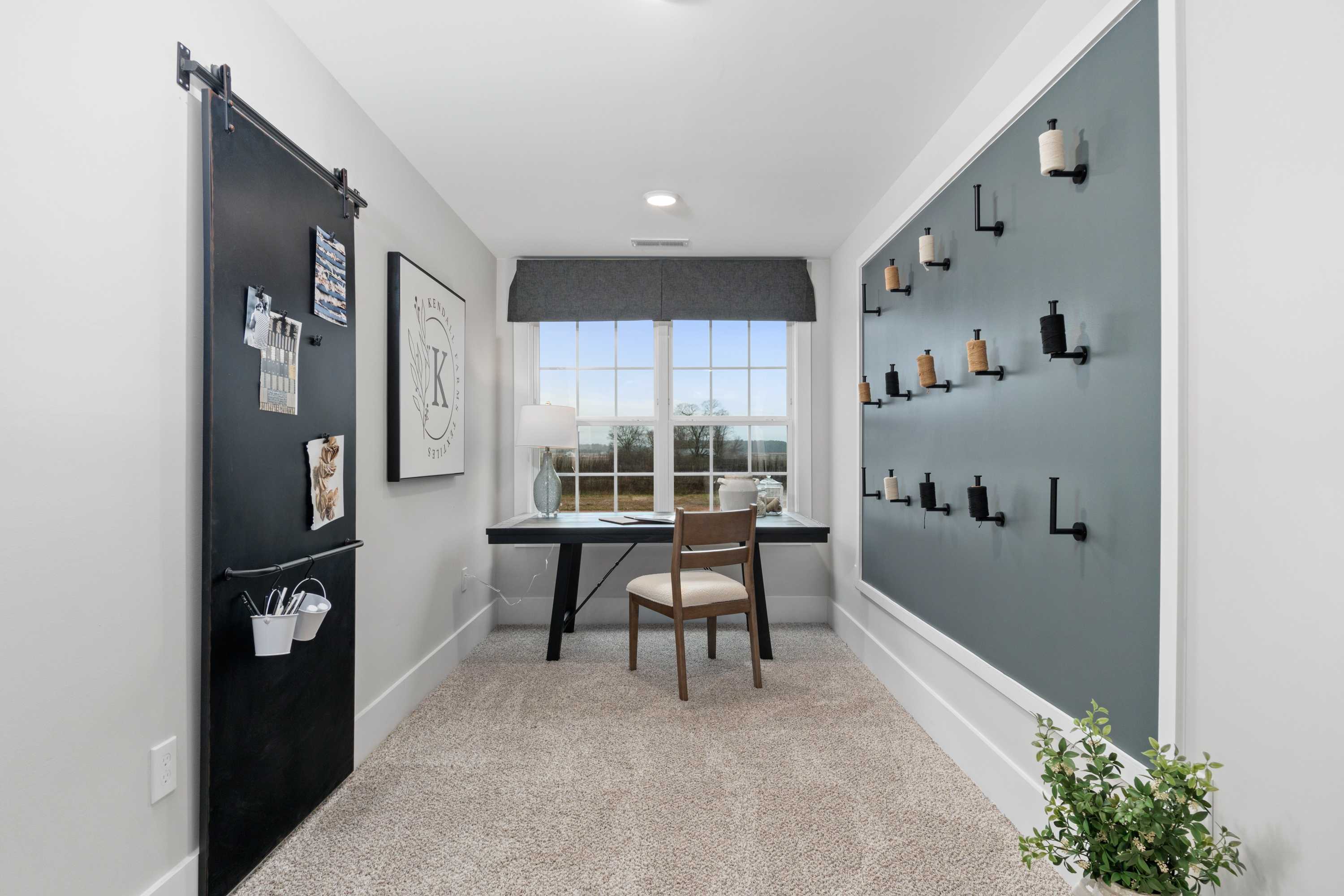 Cozy home office in Kendall Farms Toney Alabama with wooden desk, barn door, gray accent wall hooks, and potted plant