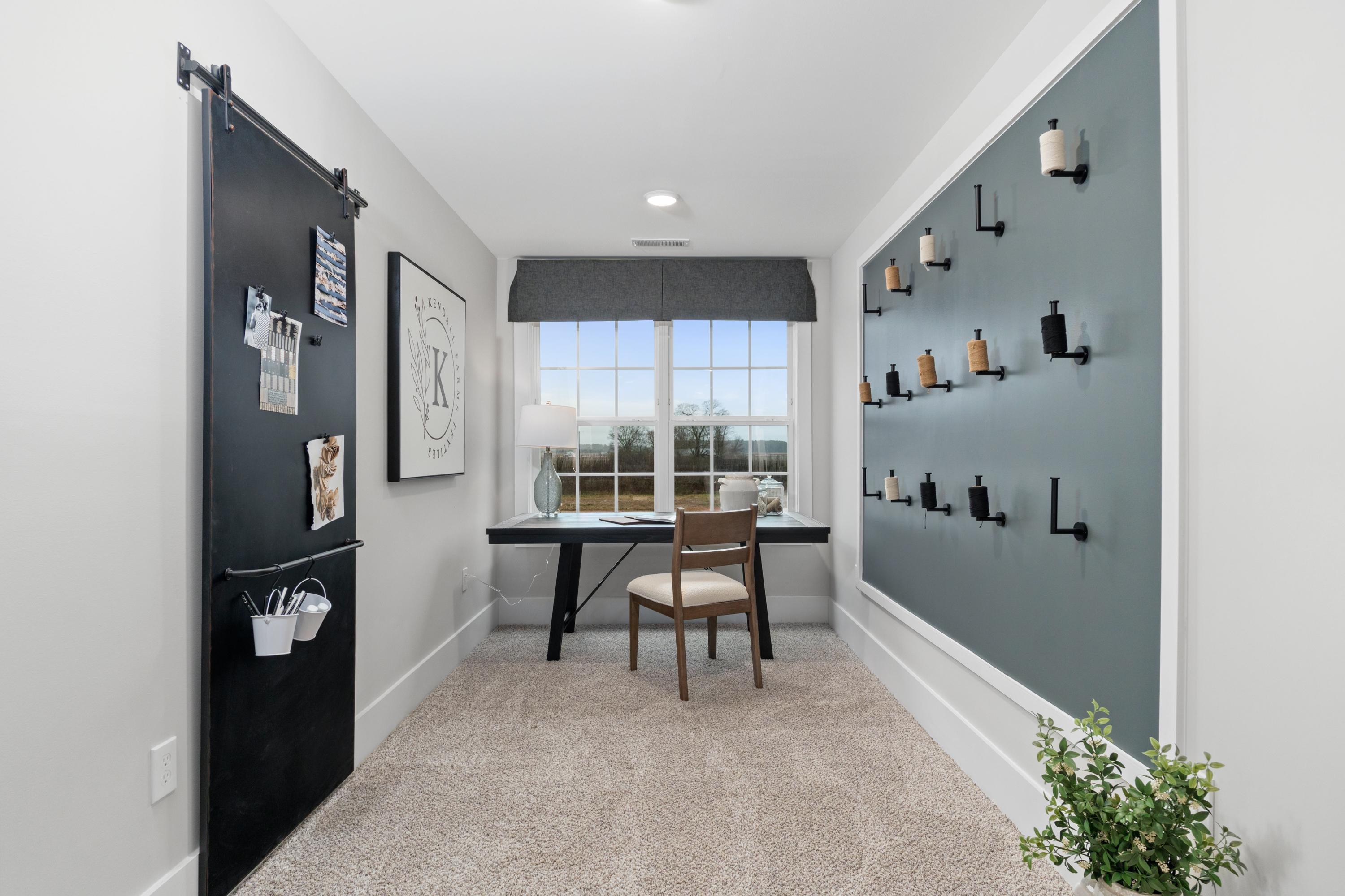 Cozy home office in Kendall Farms Toney Alabama with wooden desk, barn door, gray accent wall hooks, and potted plant