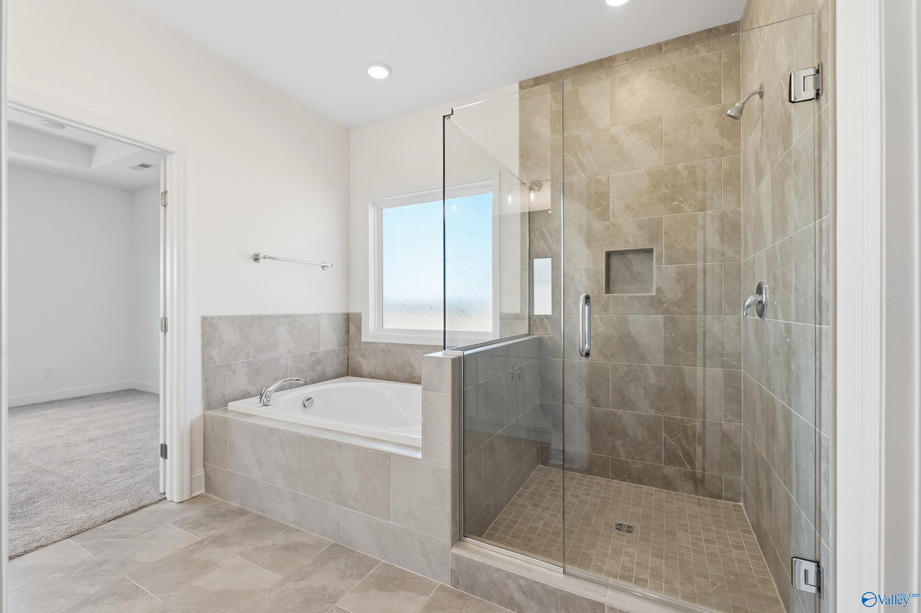 Elegant master bathroom featuring soaking tub, frameless glass shower, and beige tile in The Montgomery floor plan, Meridianville, Alabama