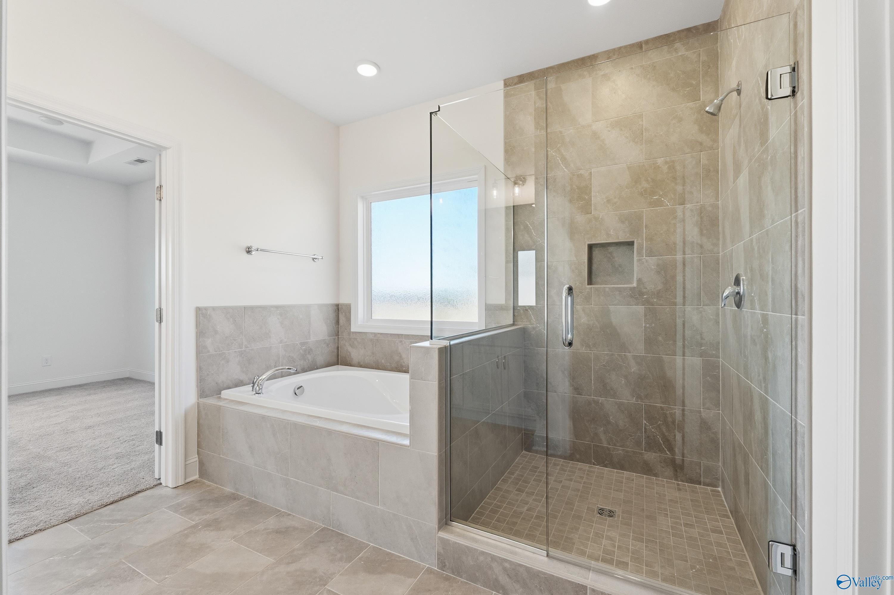 Elegant master bathroom featuring soaking tub, frameless glass shower, and beige tile in The Montgomery floor plan, Meridianville, Alabama