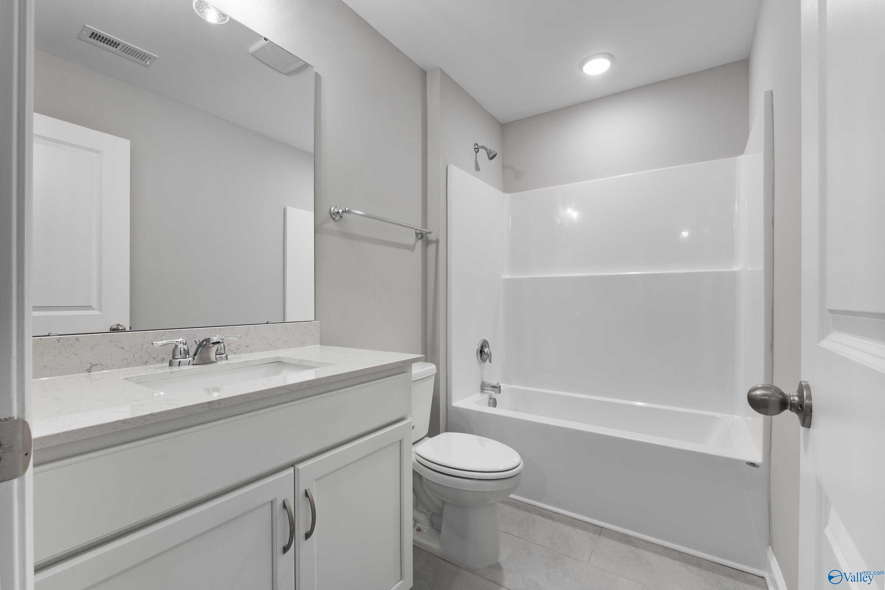 Bright bathroom with white vanity, quartz countertop, tub-shower combo in Davidson Homes The Rockford, Harvest, Alabama