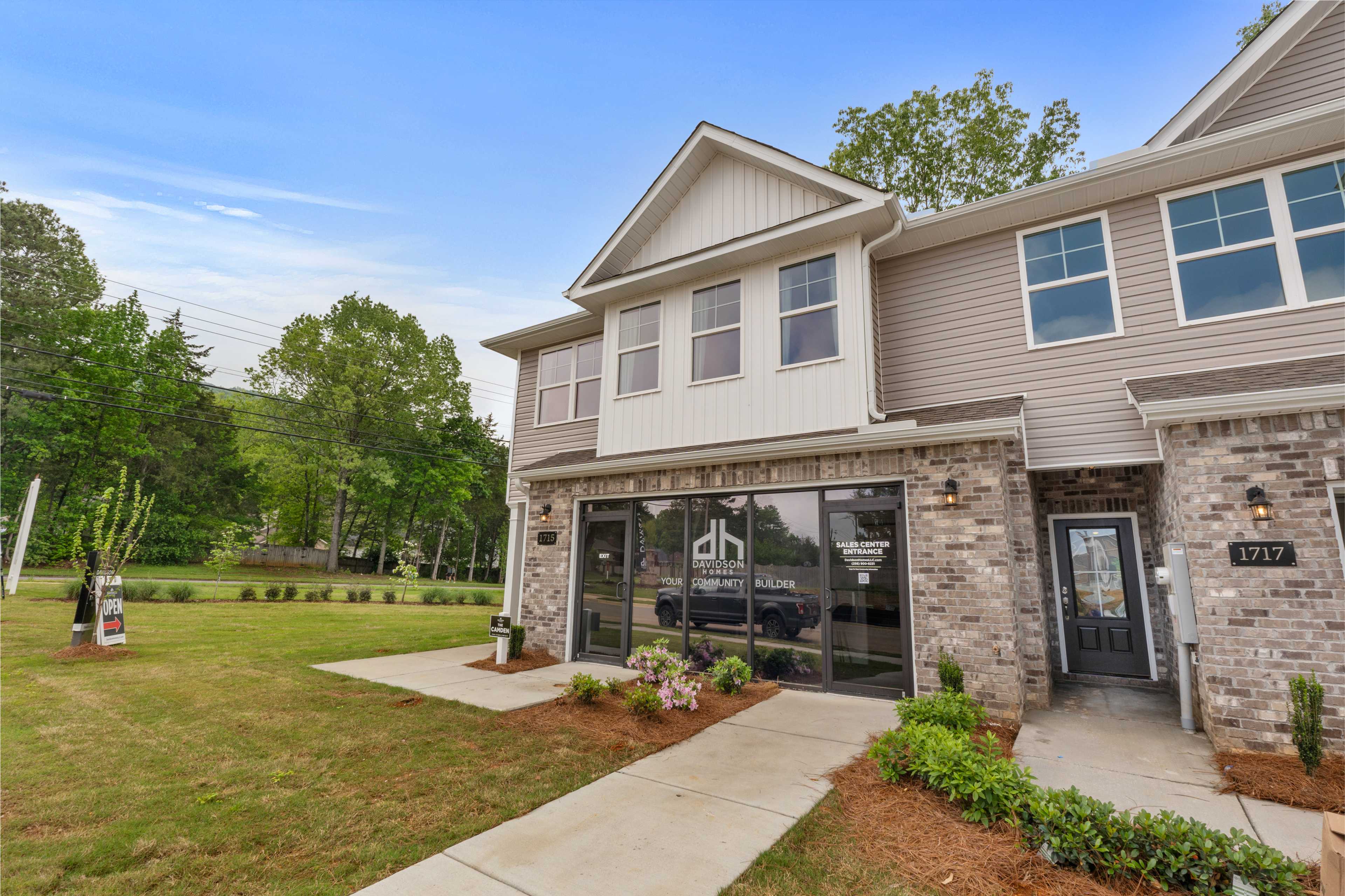 Contemporary two-story building exterior at The Pavilion in Huntsville AL with gray siding, large glass windows, brick base, and landscaped walkway