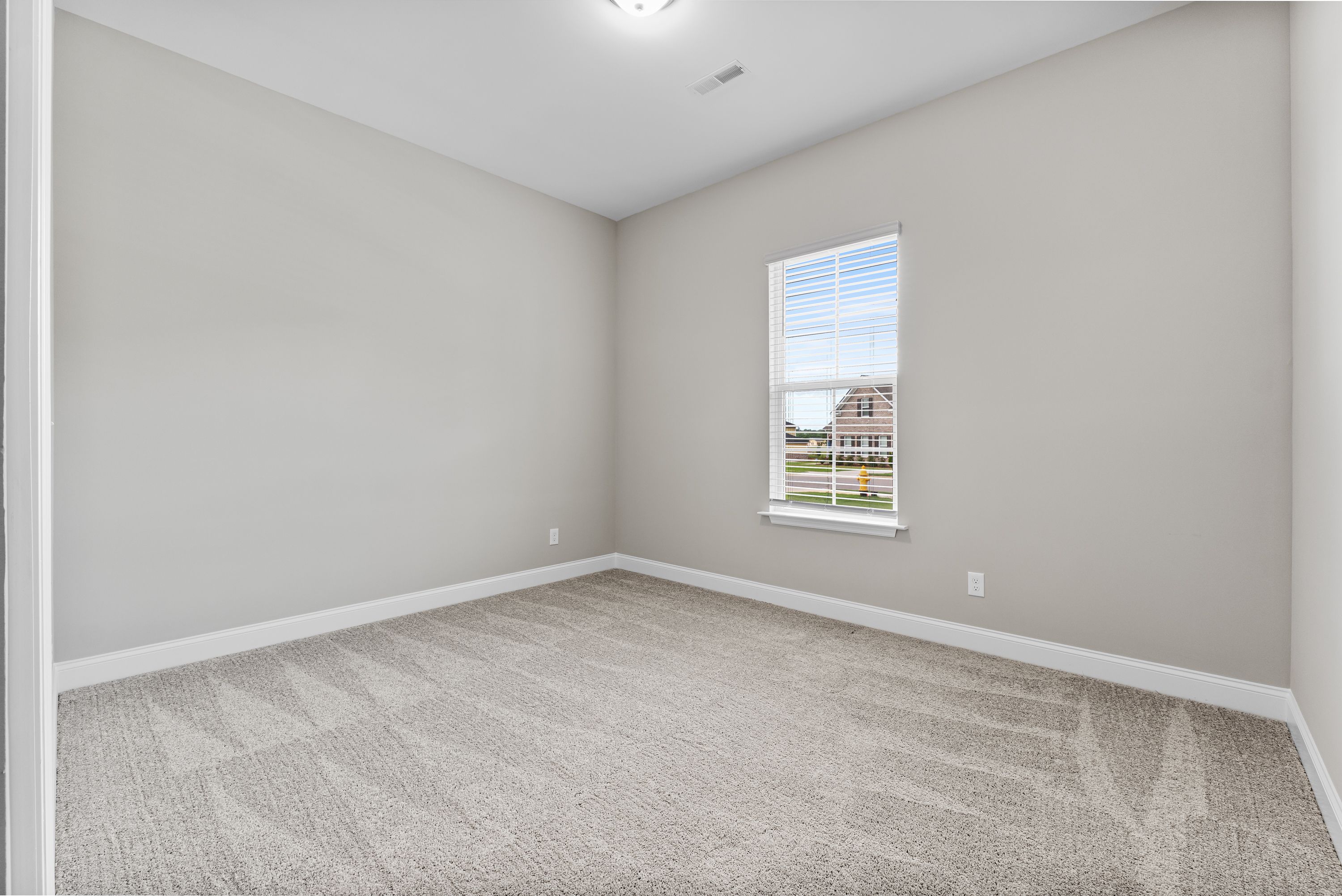 Spacious bedroom in The Arcadia E home with light gray walls, neutral carpet, and window view of suburban neighborhood