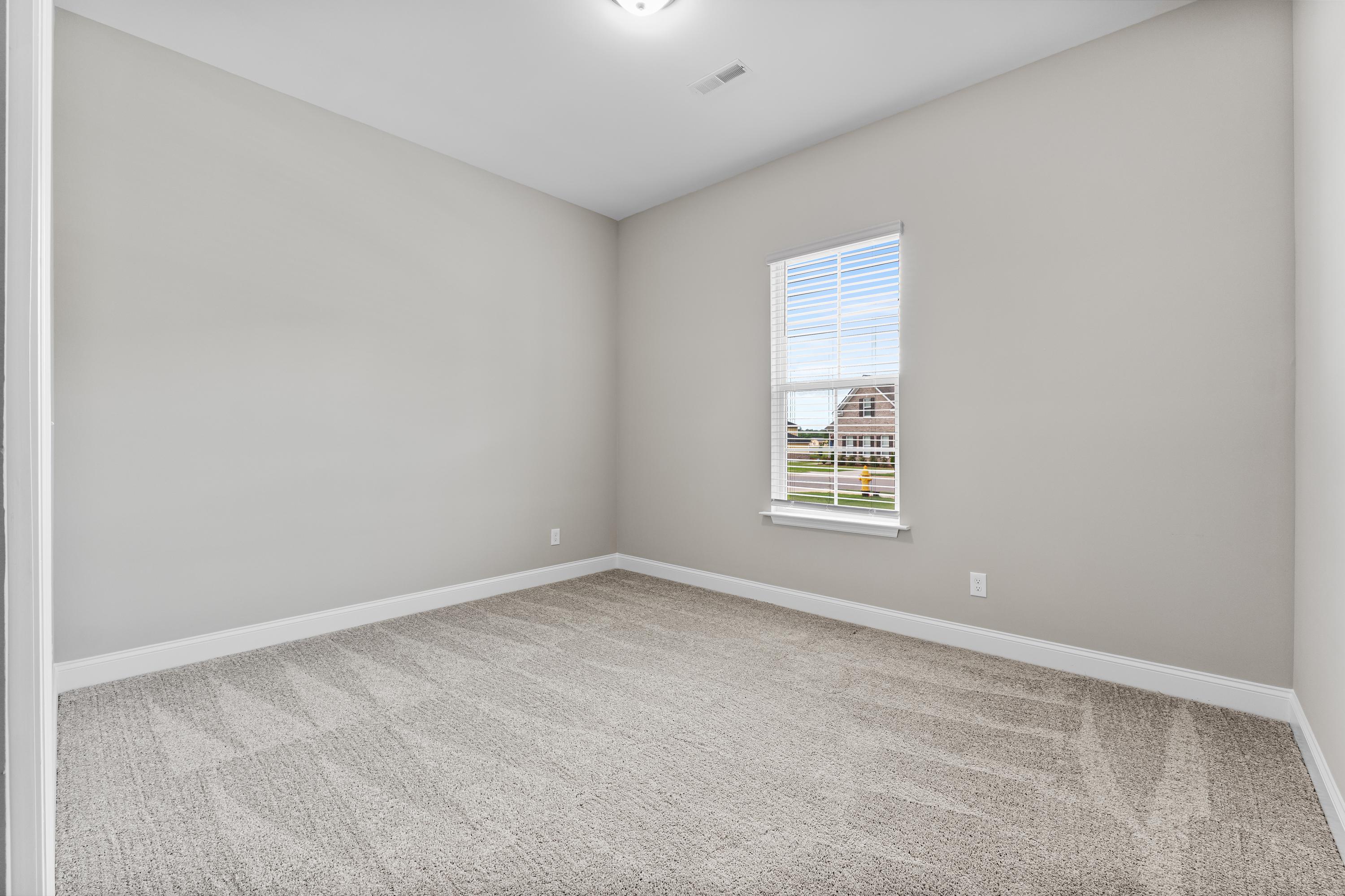 Spacious empty bedroom in The Arcadia B with light gray walls, neutral carpet, and window overlooking suburban neighborhood
