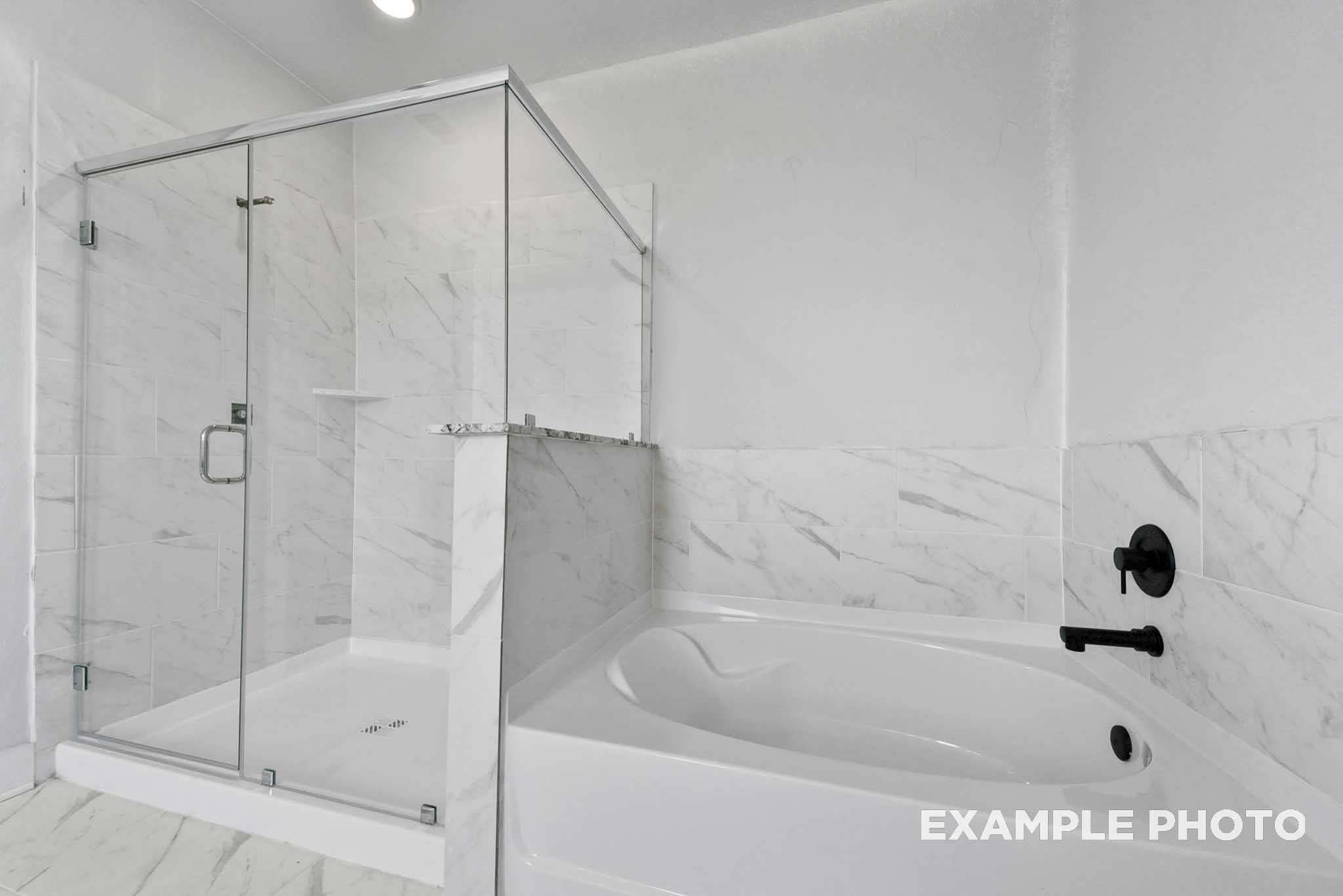Elegant master bathroom with glass shower enclosure, freestanding tub, and white marble tiles in Davidson Homes The George A, Lago Mar, Texas City