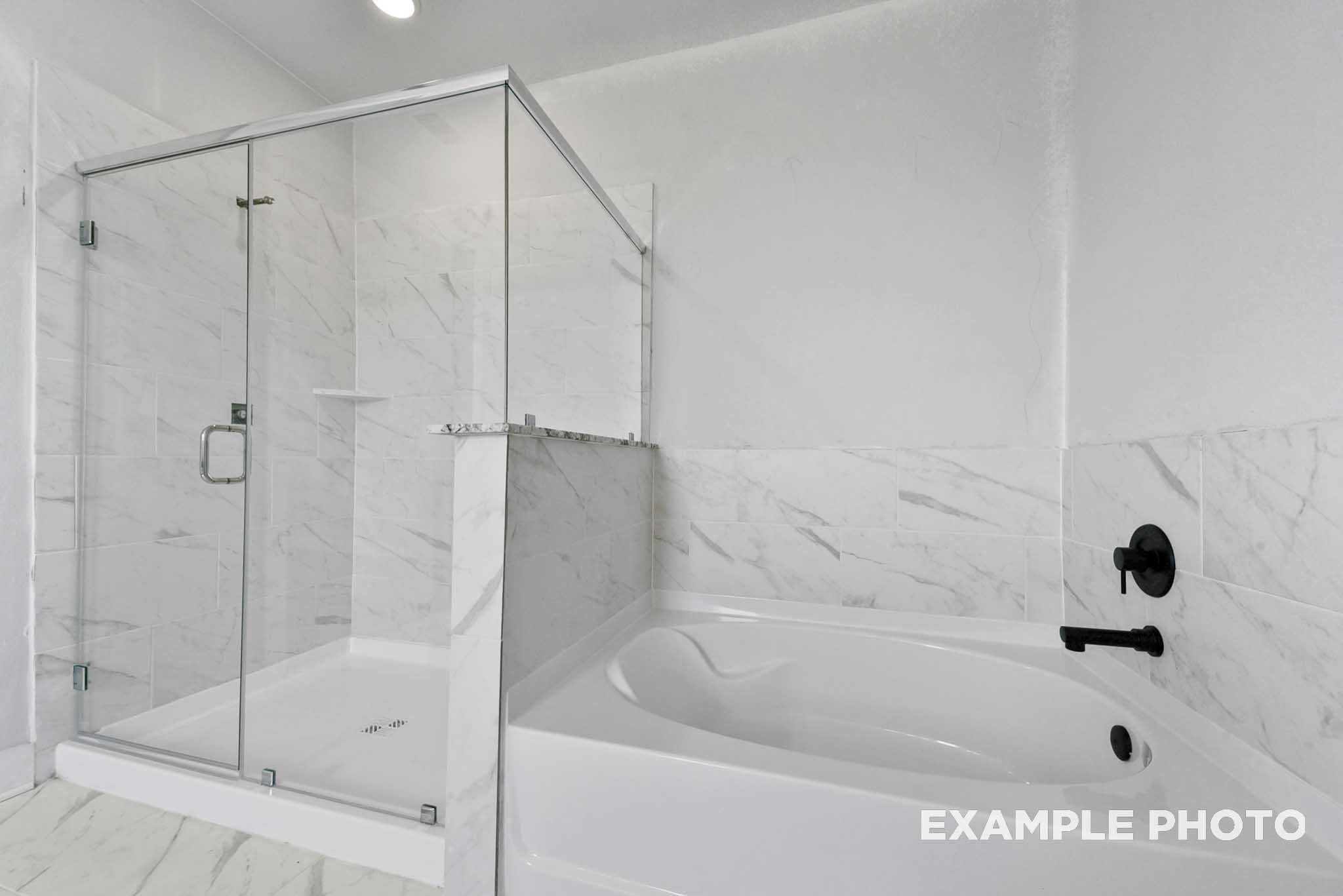 Elegant master bathroom with glass shower enclosure, freestanding tub, and white marble tiles in Davidson Homes The George A, Lago Mar, Texas City