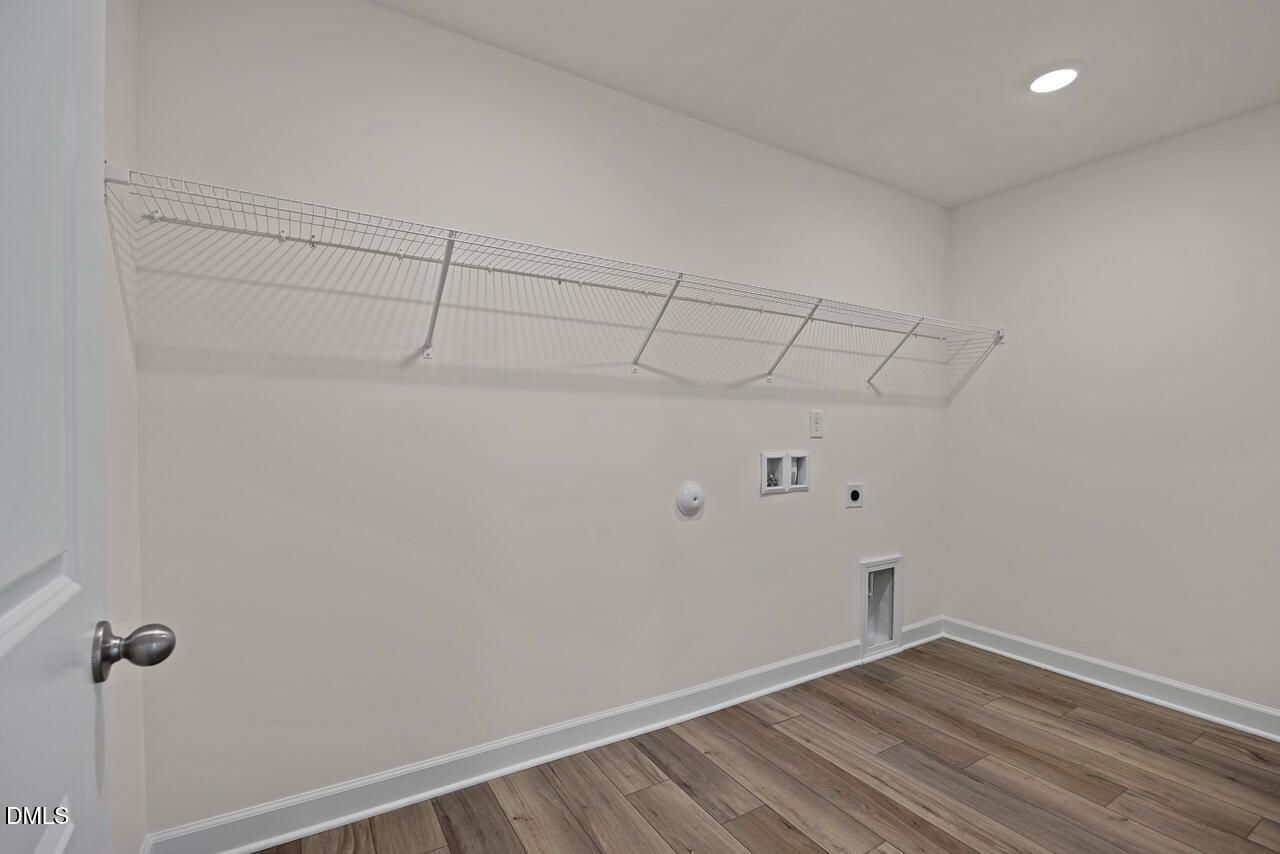 Laundry room with wire shelving, wood-look flooring, and washer connections in Davidson Homes Hickory II B, Lillington NC