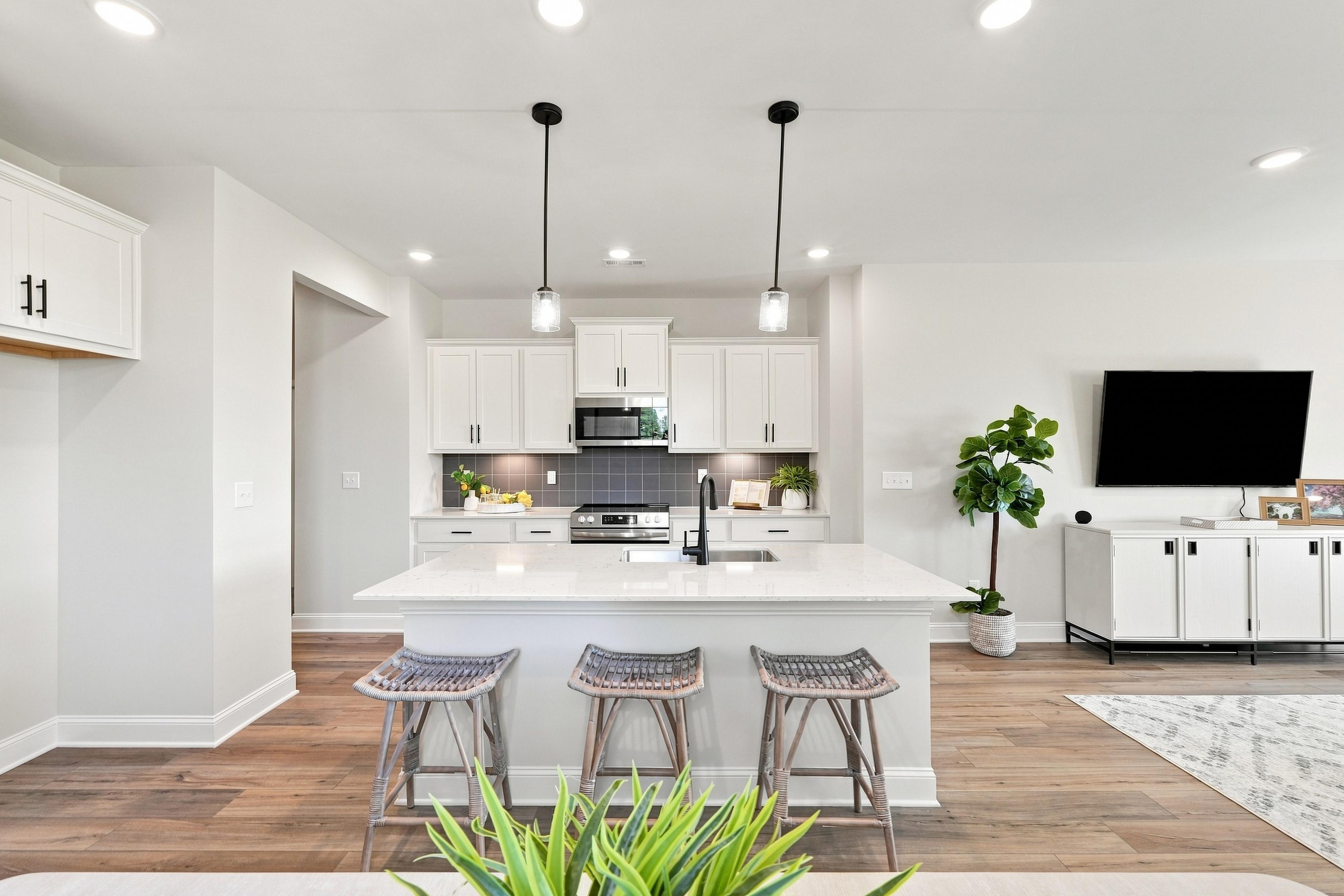White kitchen with large island, pendant lights, and bar stools in an open-concept living area at Bailey Park by Davidson Homes, Fayetteville TN