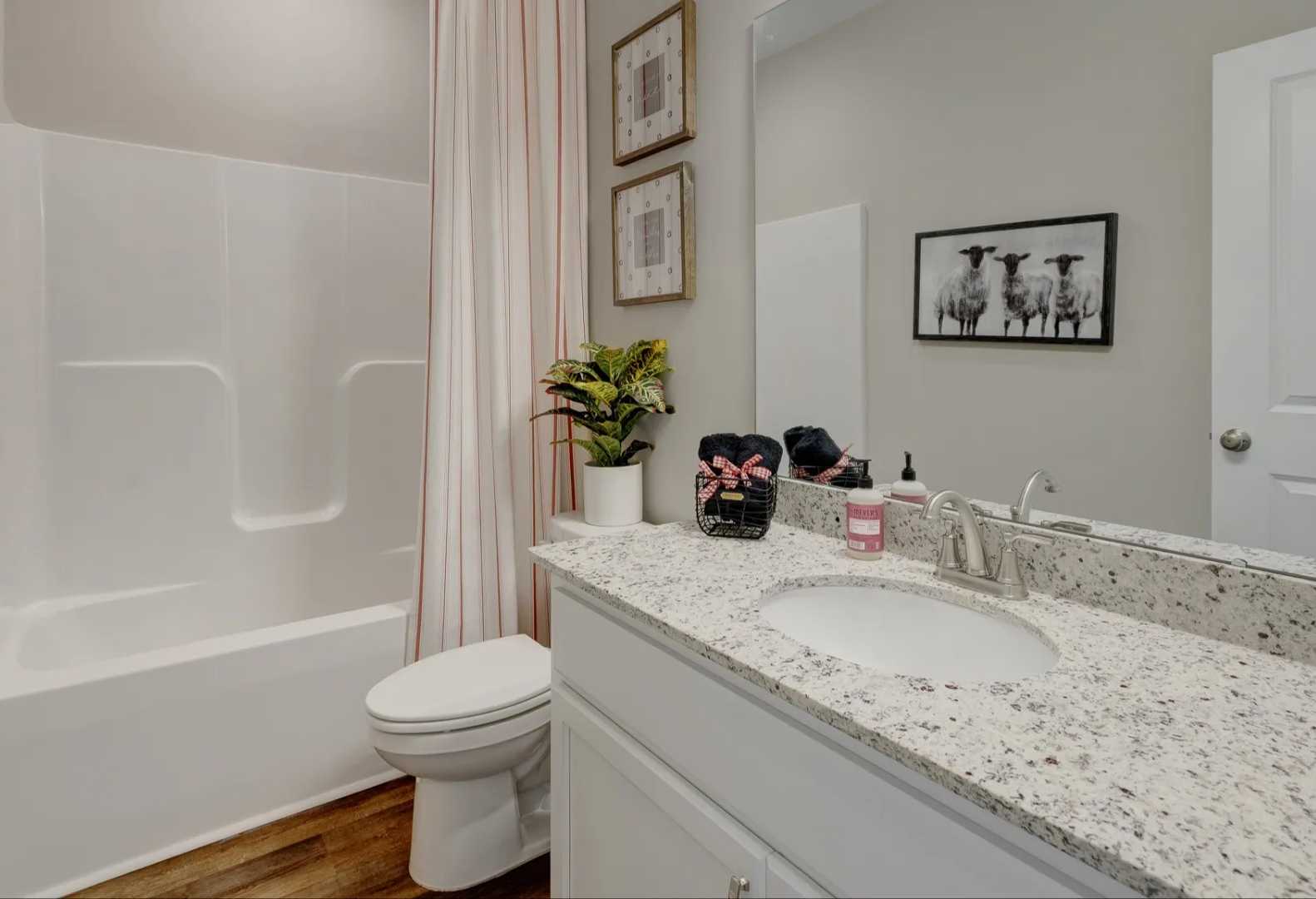 Spacious master bathroom in The Aurora A with white tub-shower combo, quartz vanity, neutral walls and wood floors