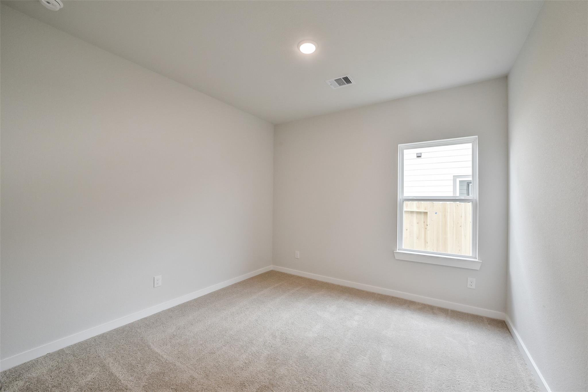 Spacious empty bedroom with neutral walls, carpet flooring, and window view in Davidson Homes The Frio F, Conroe, TX