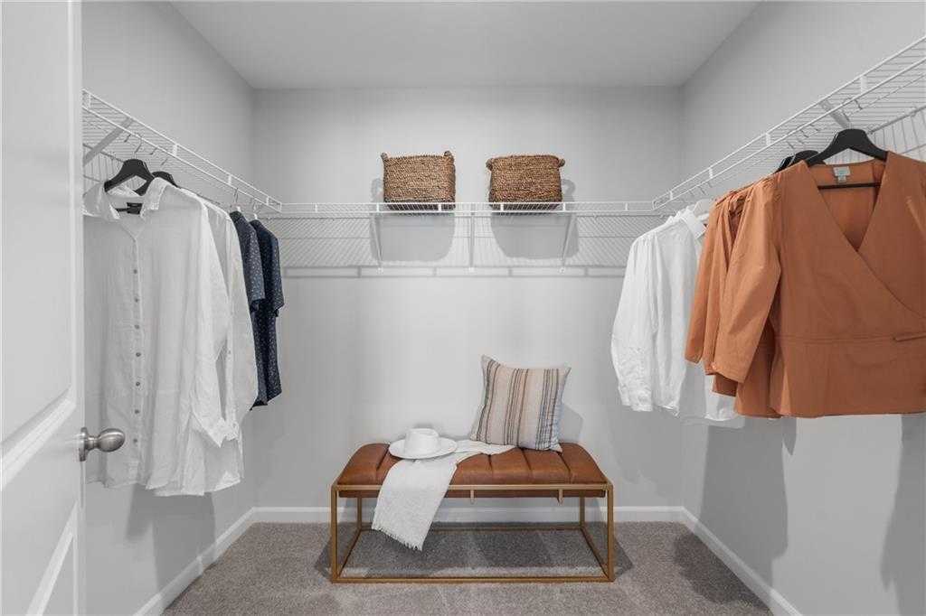 Spacious walk-in closet with wire shelving, hanging clothes, wicker baskets, and upholstered bench in Davidson Homes The Durant A, Emerson, Georgia