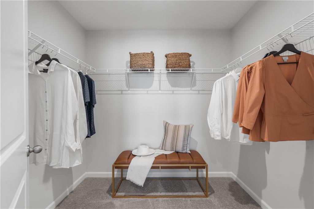 Spacious walk-in closet with wire shelving, hanging clothes, wicker baskets, and tufted bench in Davidson Homes The Durant A, Emerson, Georgia
