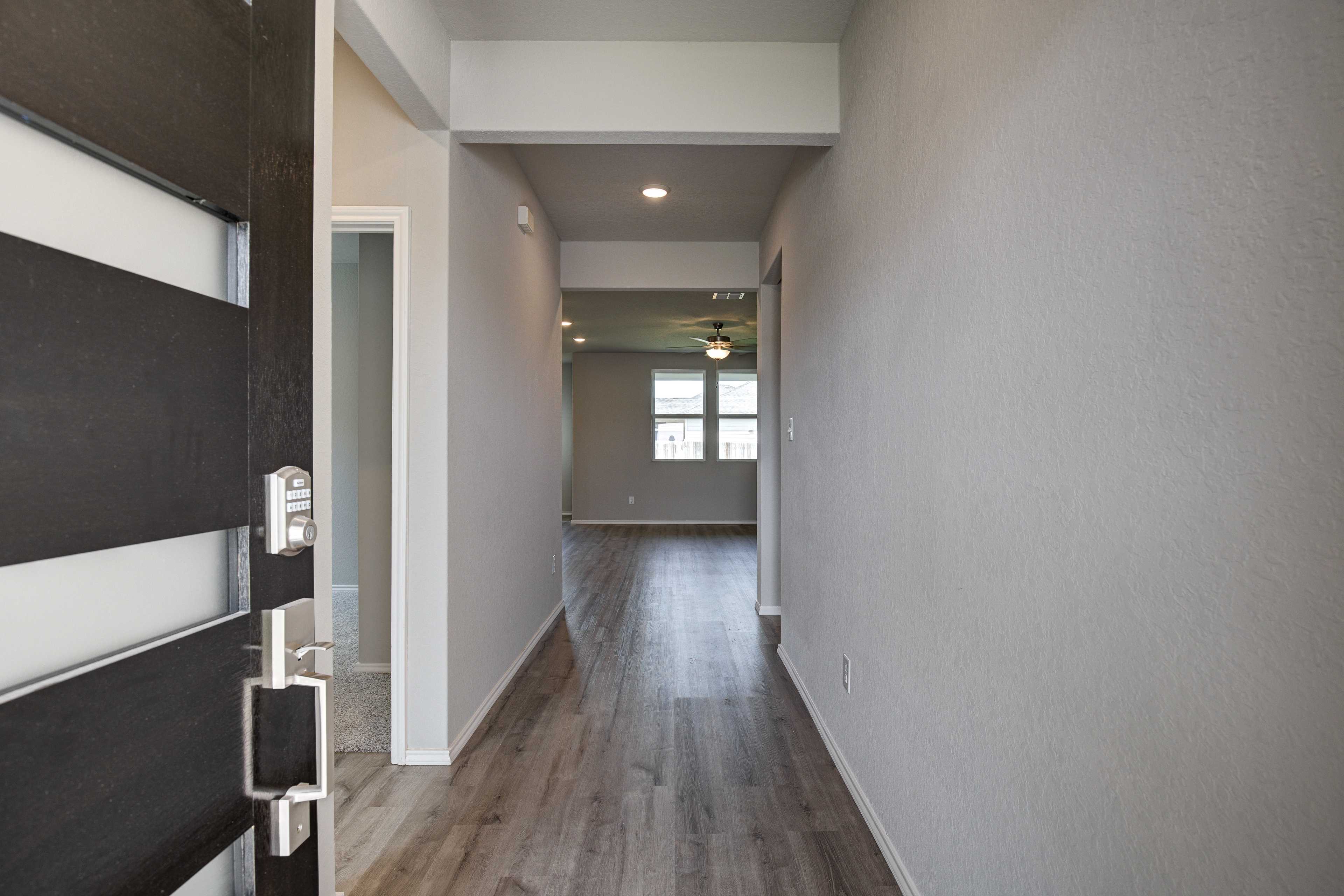 Spacious entry hallway in The Asheville home design with modern black door, light hardwood floors, and open living area by Davidson Homes in Seguin Texas