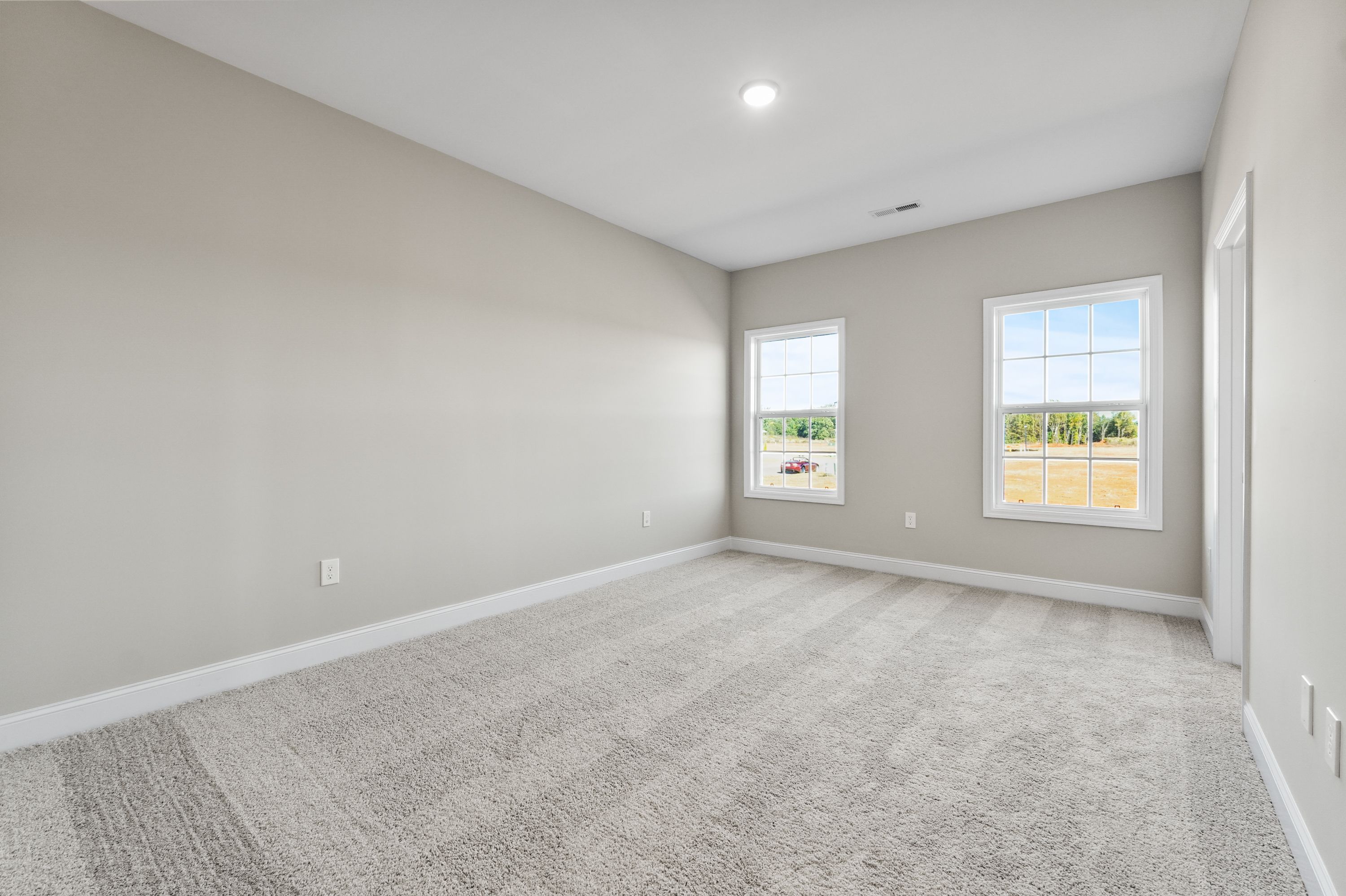 Spacious secondary bedroom in The Valencia home with beige walls, gray carpet, large windows overlooking rural fields