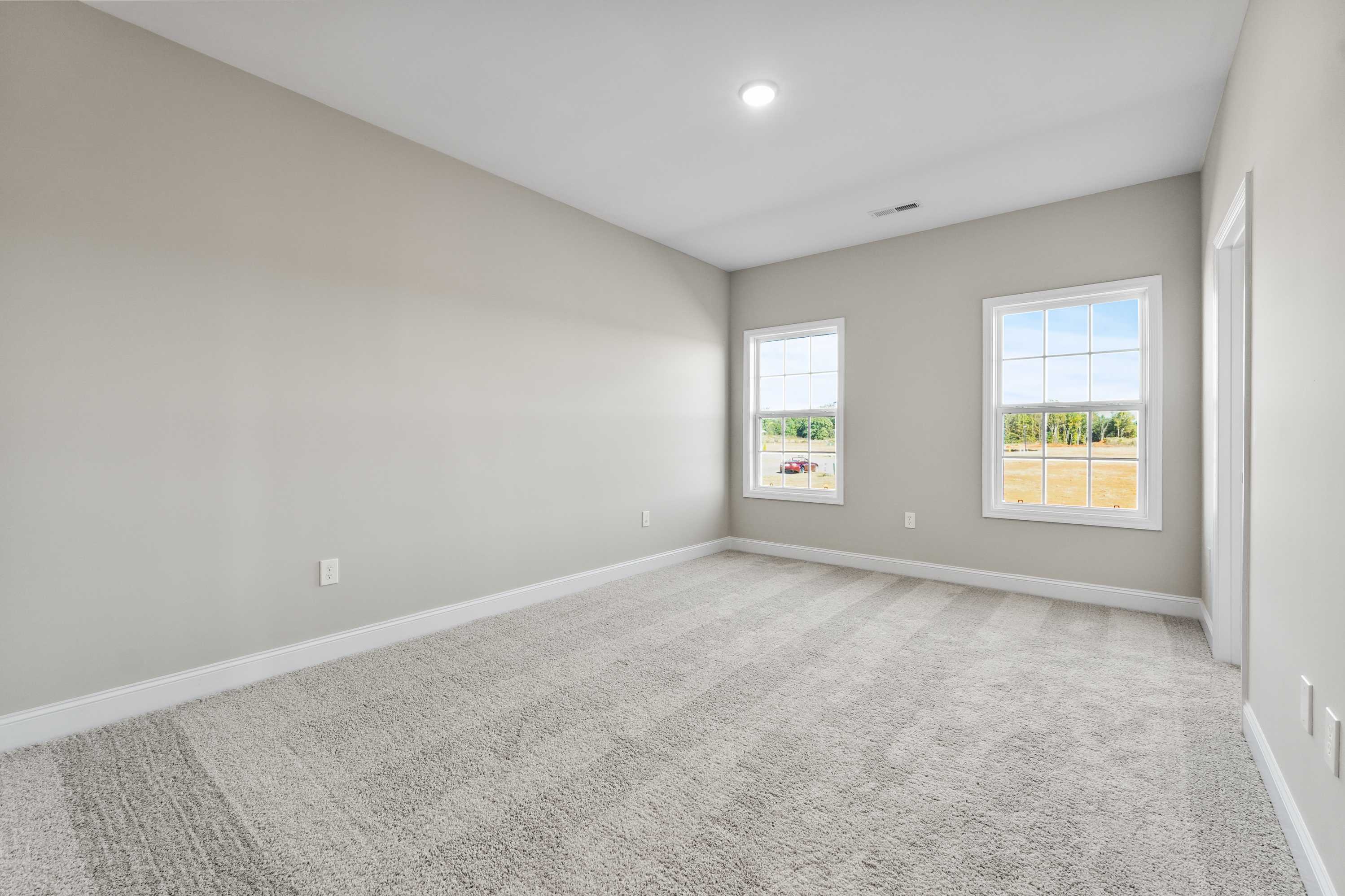 Spacious secondary bedroom in The Valencia home with beige walls, gray carpet, large windows overlooking rural fields