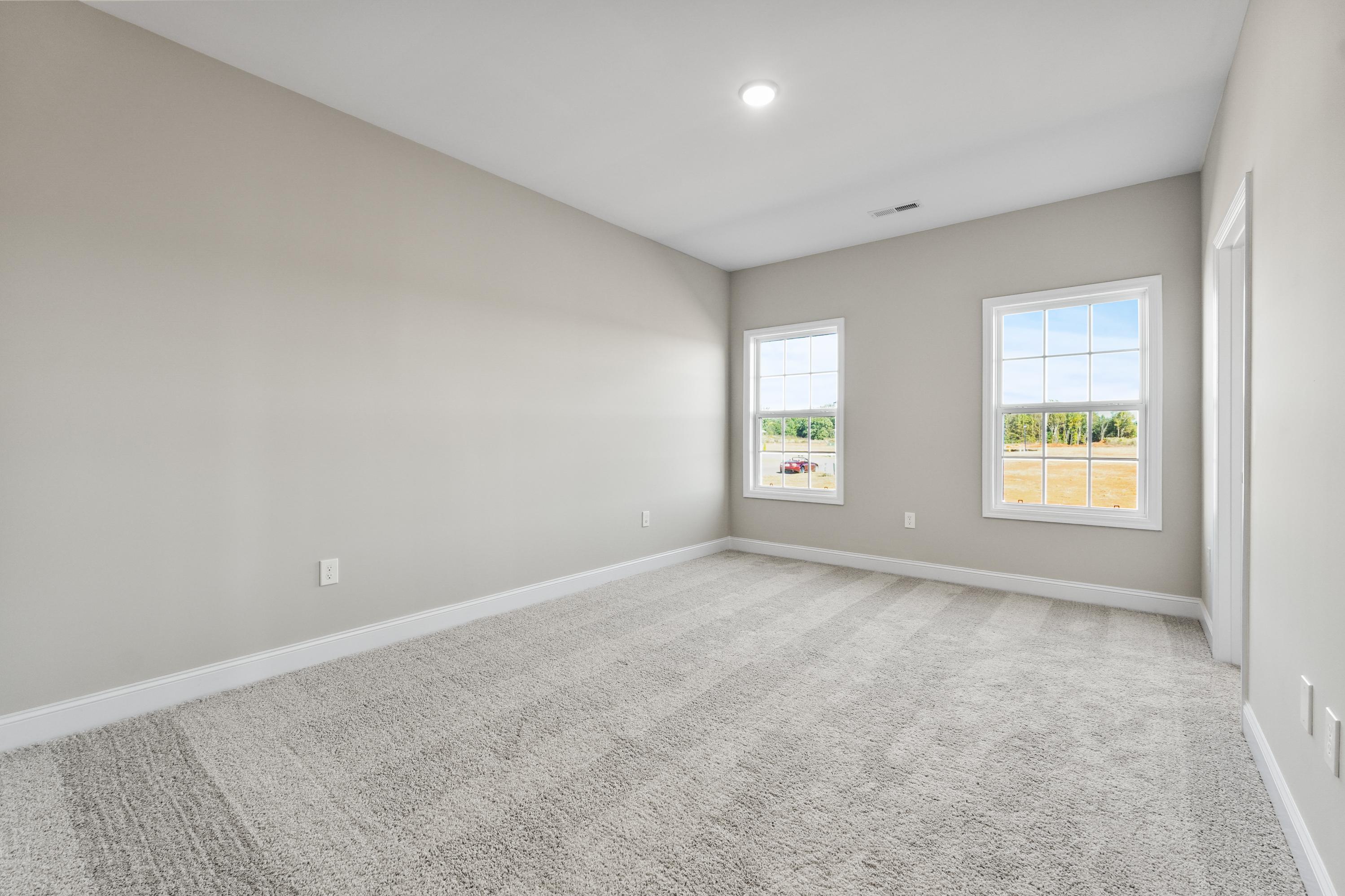 Spacious secondary bedroom in The Valencia home with beige walls, gray carpet, large windows overlooking rural fields