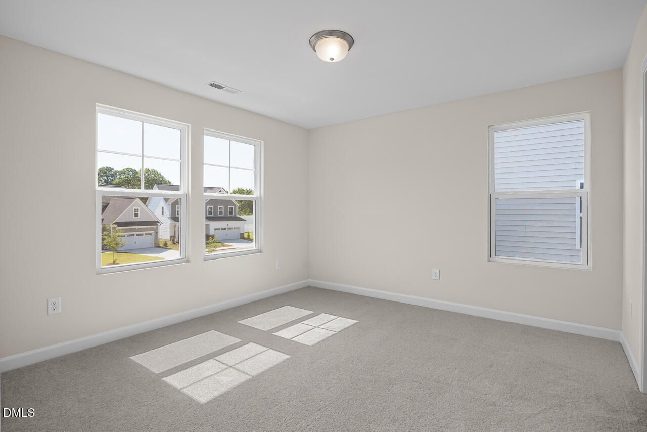 Bright carpeted bedroom with large windows overlooking homes in Woodland Crossing, Zebulon, NC — Davidson Homes The Willow C plan