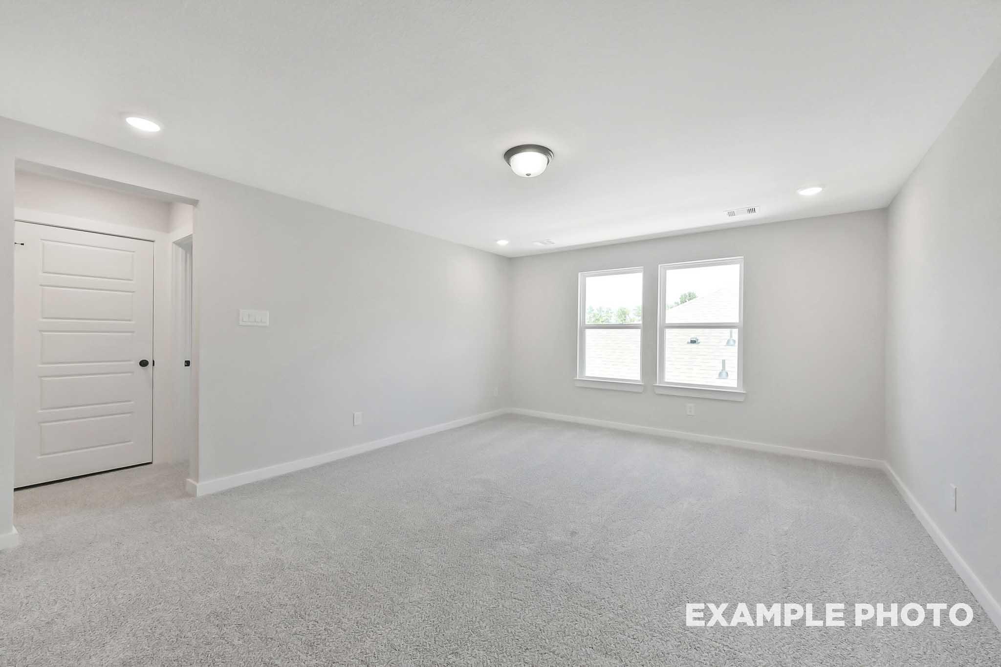 Spacious empty bedroom in The Sequoia home with gray carpet, white walls, large windows, and recessed lighting