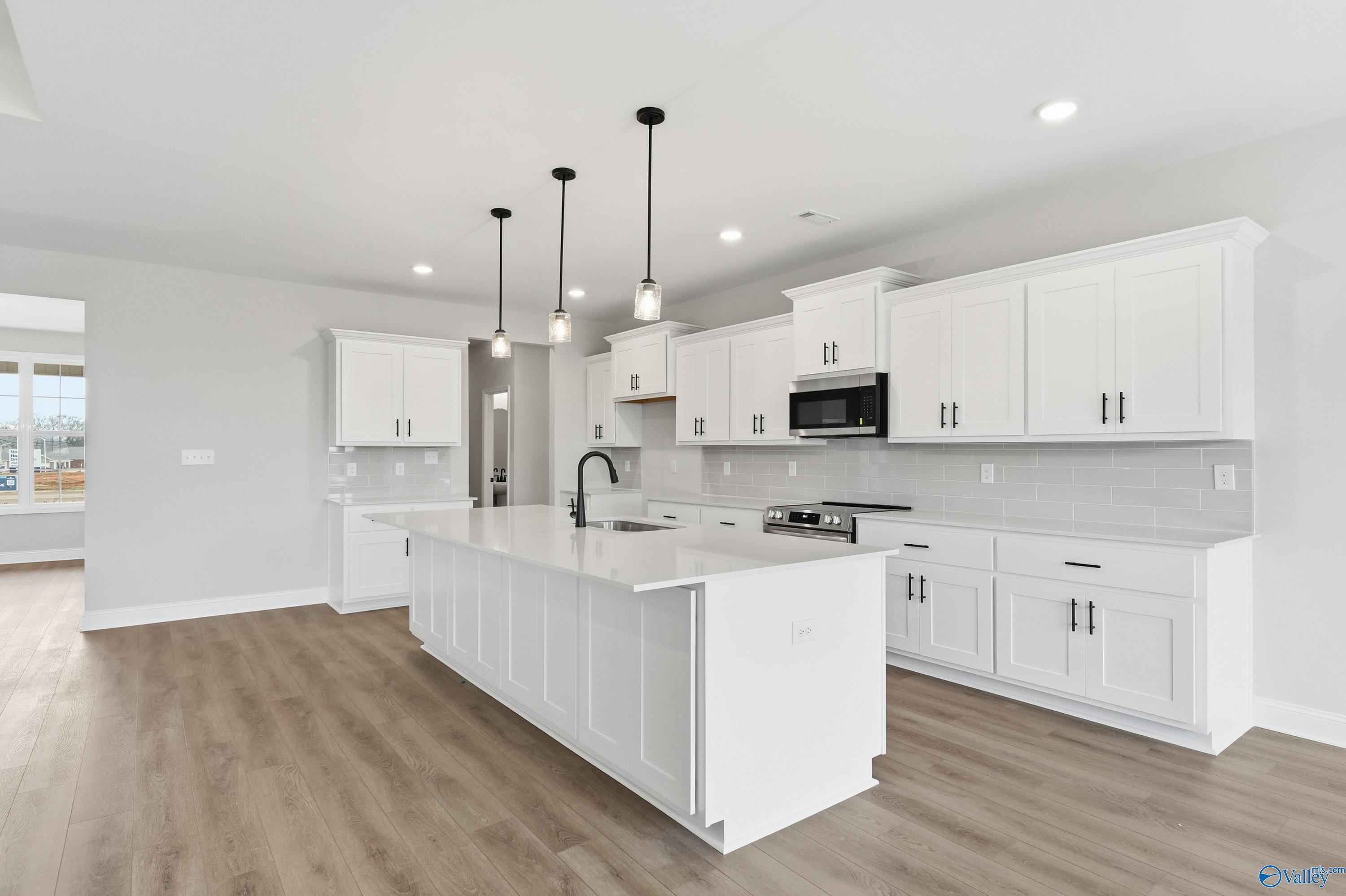 Modern white shaker kitchen with large island, stainless appliances, pendant lights in The Finleigh by Davidson Homes, Meridianville, AL