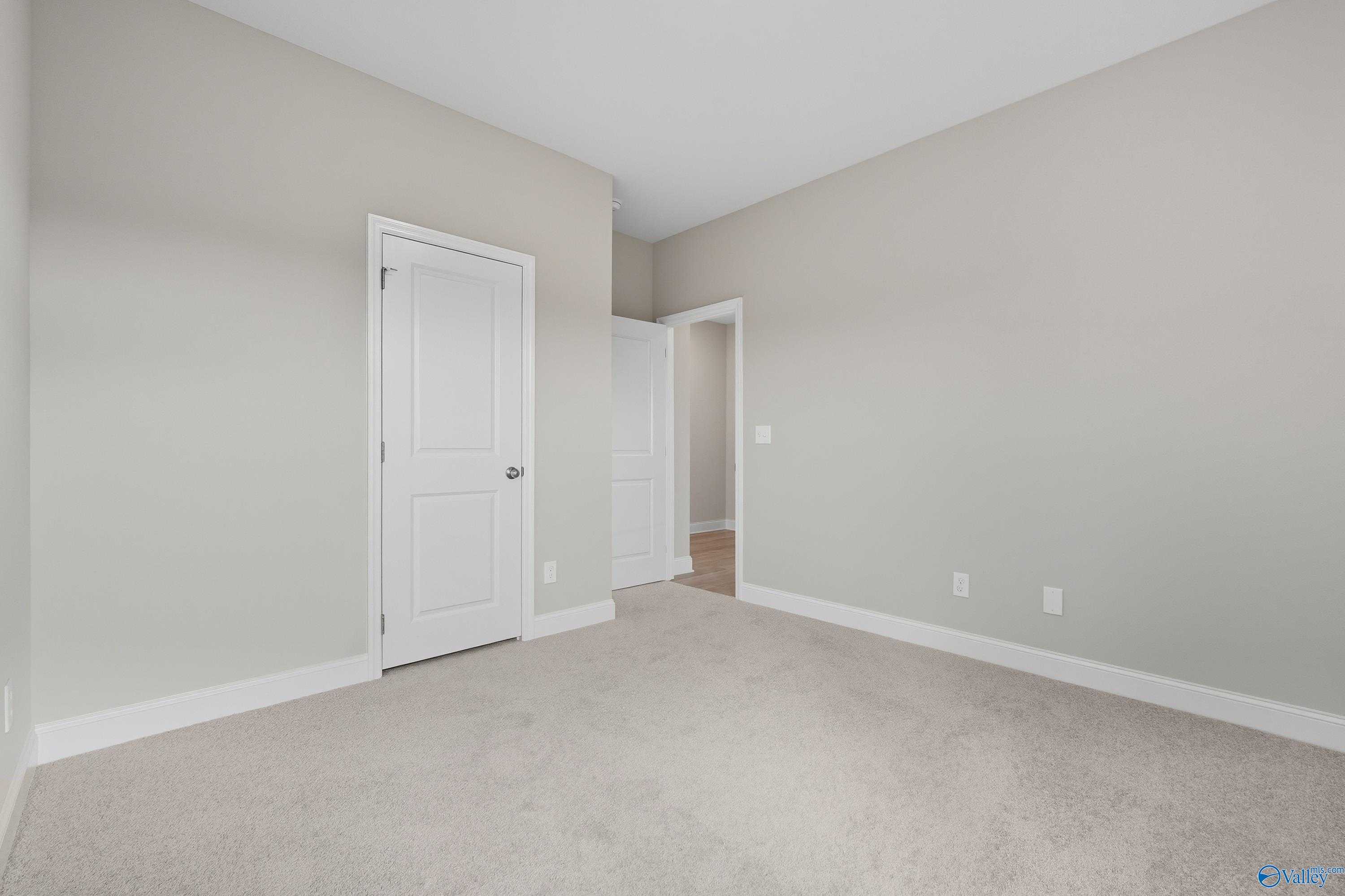 Empty secondary bedroom featuring beige walls, white doors, and neutral carpet in Davidson Homes The Franklin, Meridianville, AL