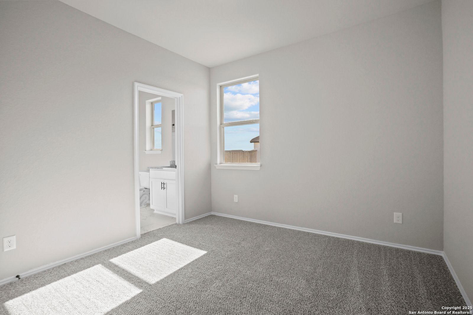 Spacious secondary bedroom with gray carpet, attached bath vanity and window view in The Daphne H, Seguin, Texas