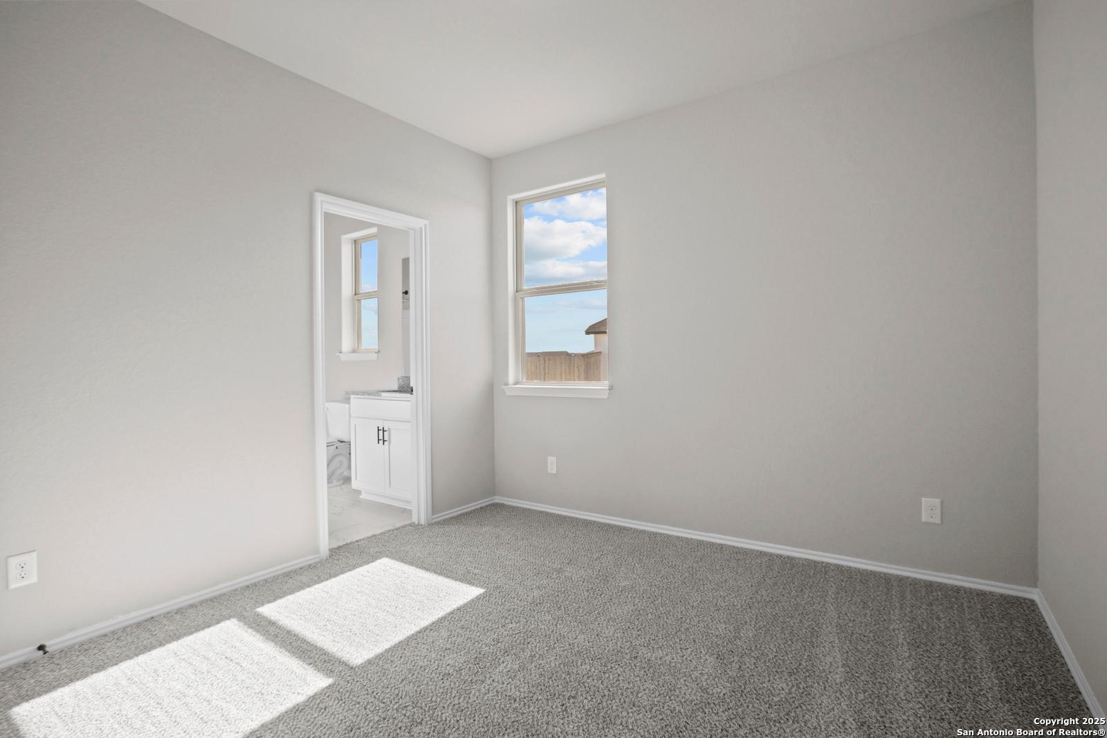 Spacious secondary bedroom with gray carpet, attached bath vanity and window view in The Daphne H, Seguin, Texas