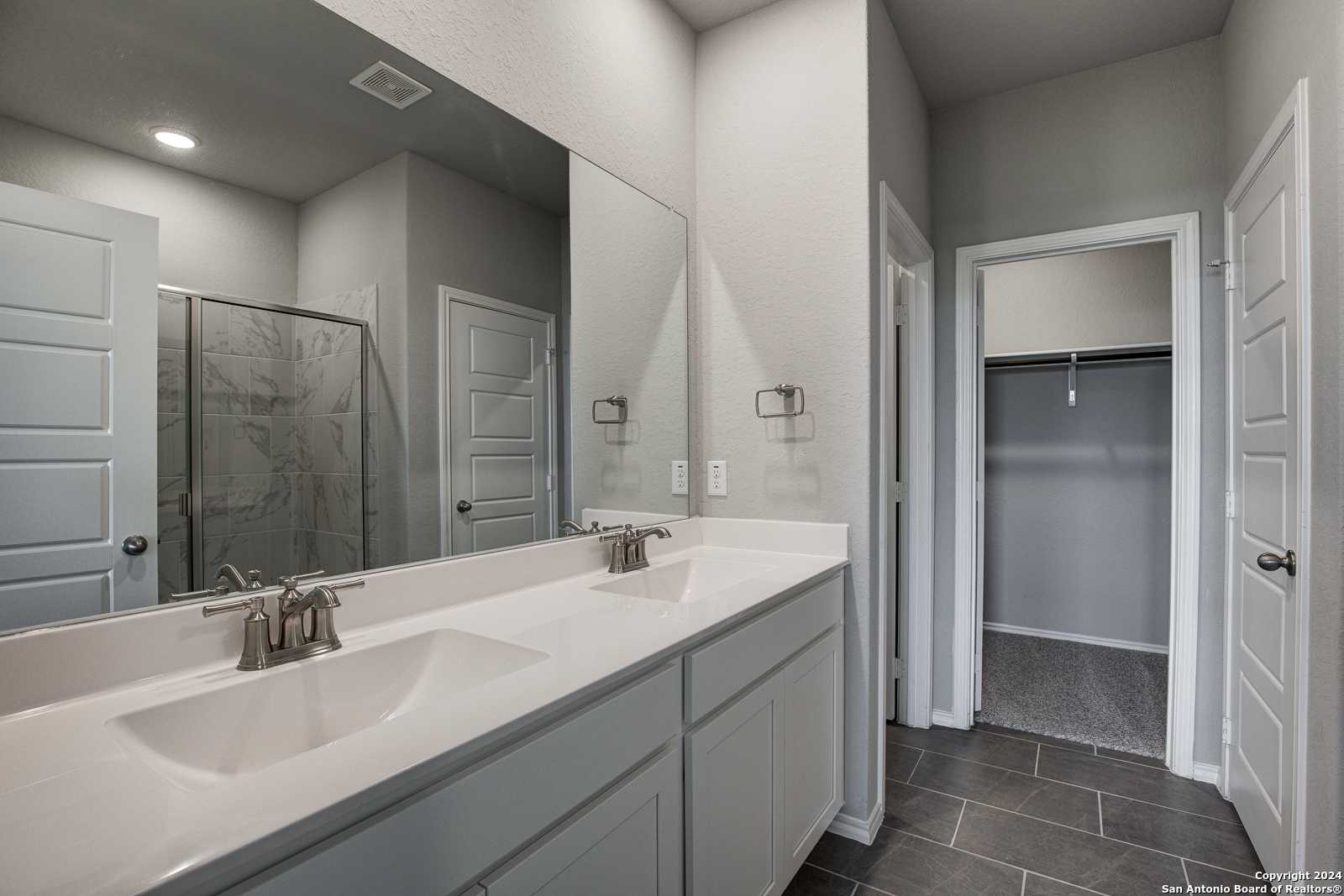 Spacious master bathroom featuring double vanity, frameless walk-in shower, and adjacent closet in Davidson Homes The Daphne J, Seguin, Texas