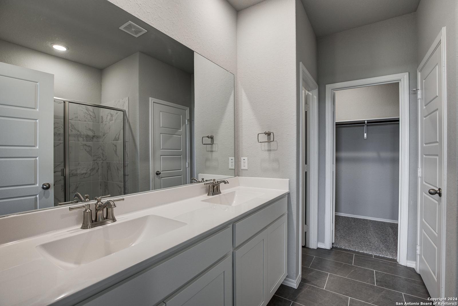 Spacious master bathroom featuring double vanity, frameless walk-in shower, and adjacent closet in Davidson Homes The Daphne J, Seguin, Texas