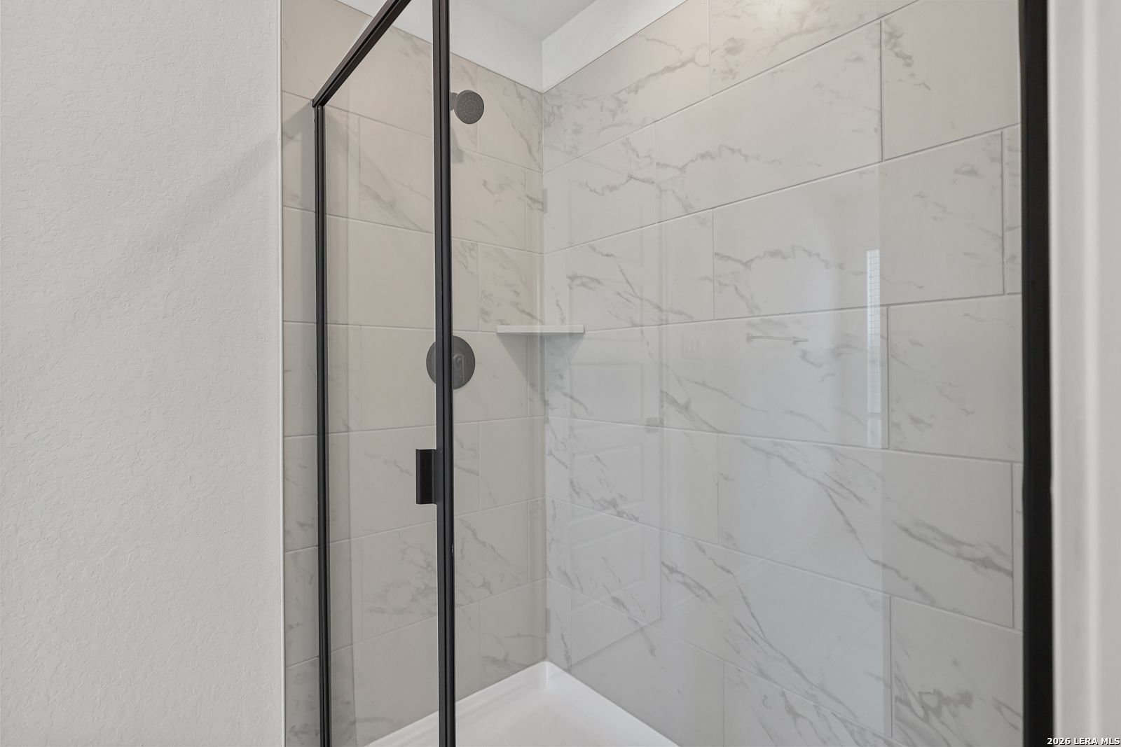 Modern walk-in shower with marble-look tile and black frame in The Gillian C home at Meadows at Oak Creek, San Antonio.