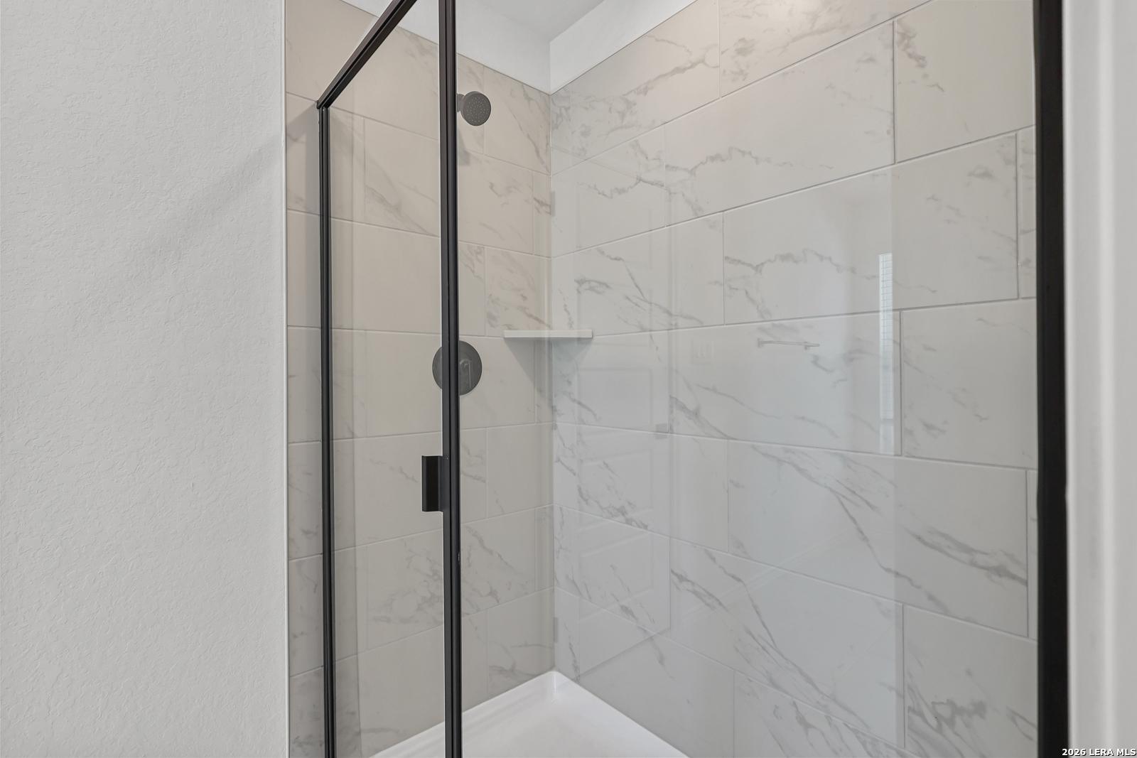 Modern walk-in shower with marble-look tile and black frame in The Gillian C home at Meadows at Oak Creek, San Antonio.