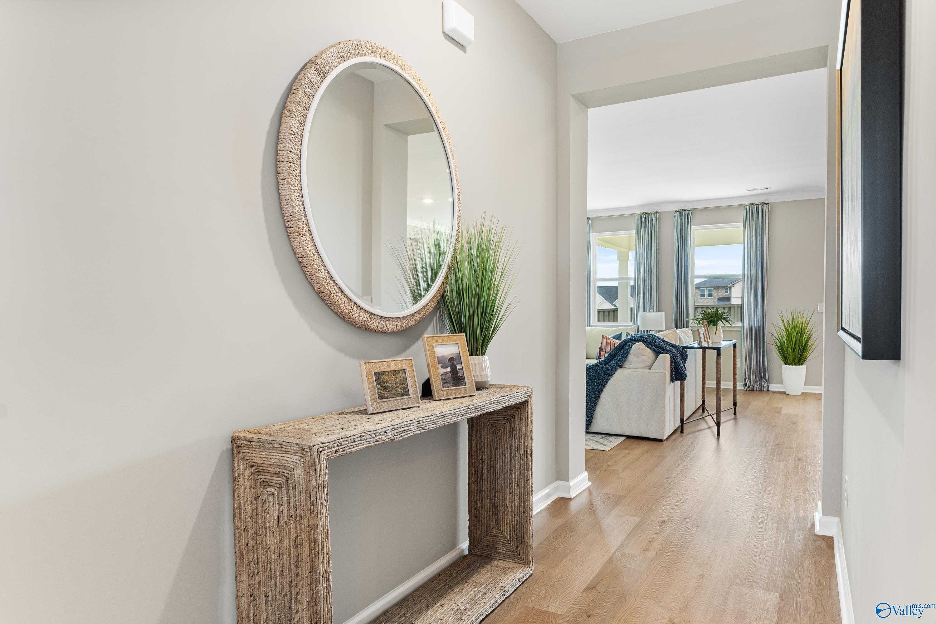 Elegant hallway with round woven mirror, wooden console table, plants, and open view to living room in Davidson Homes The Sanctuary, Athens AL