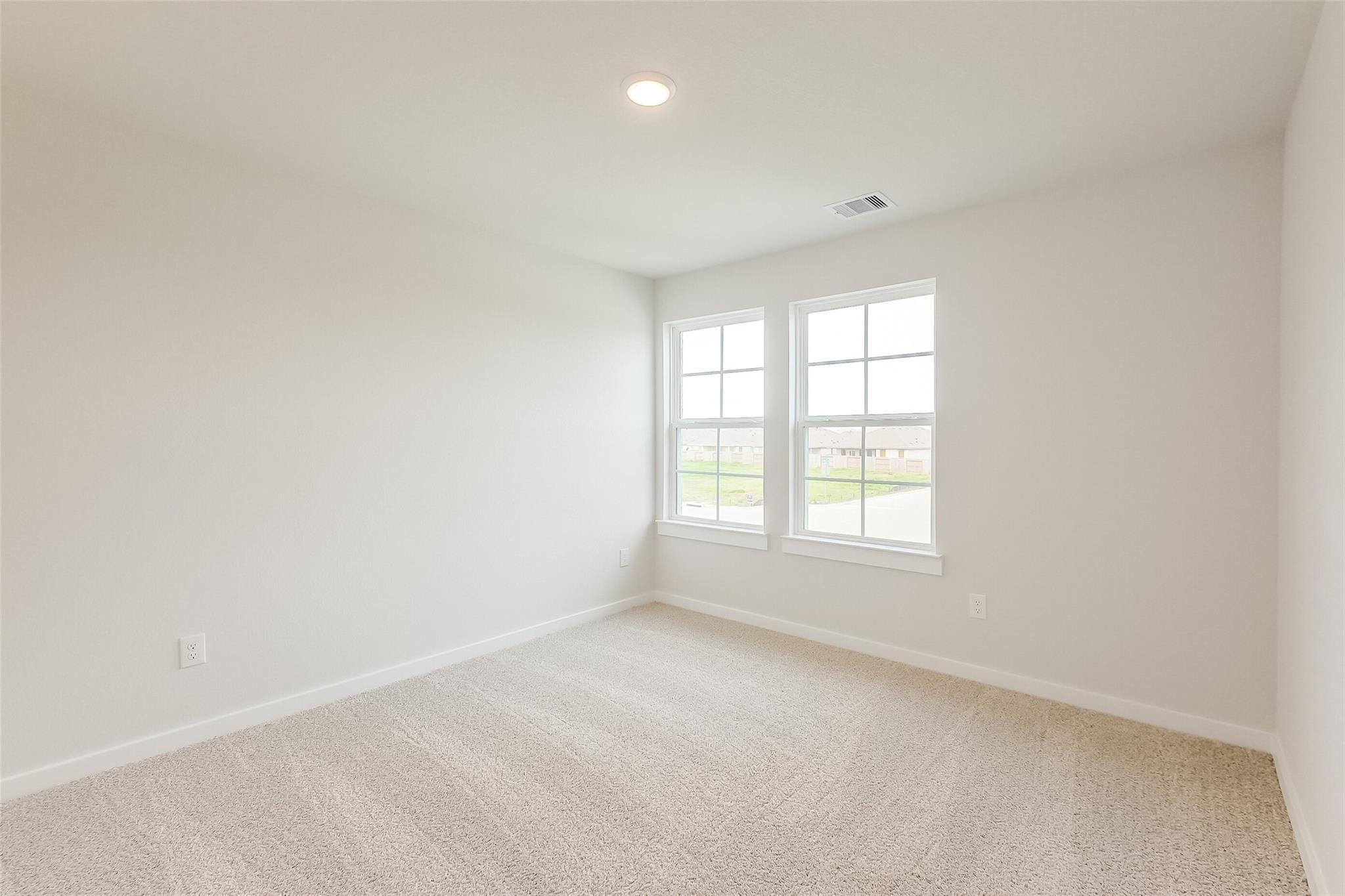 Bright empty bedroom with white walls, beige carpet, large windows overlooking green space in Davidson Homes The Tierra B, Beasley, Texas
