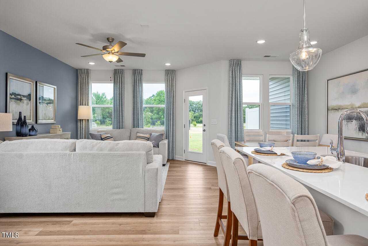 Spacious open living and dining area with gray sectional sofa, wooden floors, and sliding doors to backyard in Davidson Homes The Graham, Fuquay-Varina, NC