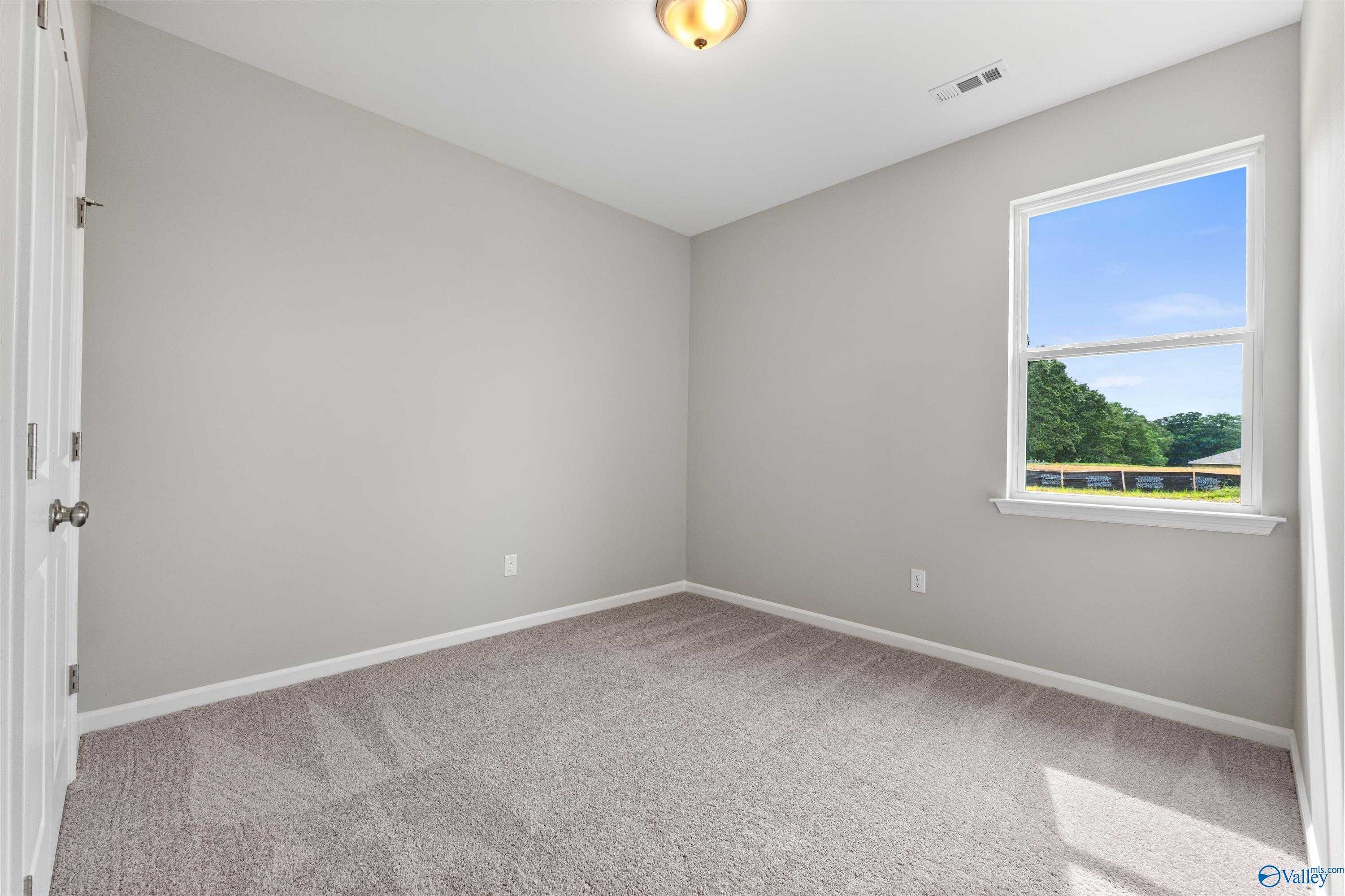 Bright empty bedroom with gray walls, neutral carpet, and large window overlooking trees in The Aurora 4-bedroom home, Fayetteville, TN