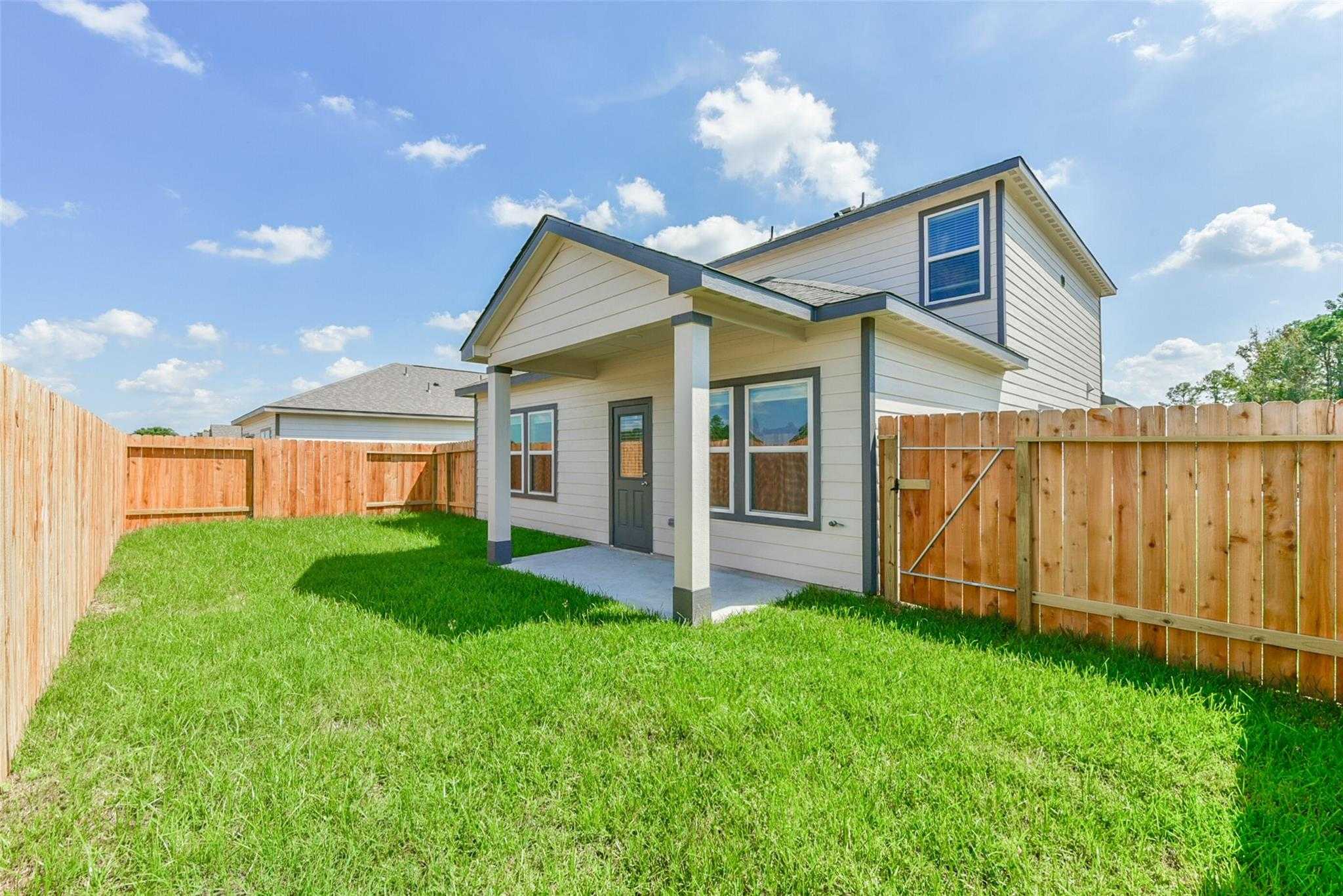 Two-story Sabine E home exterior with covered porch, large windows, and fenced green yard in The Villages at WestPointe, Dayton, Texas