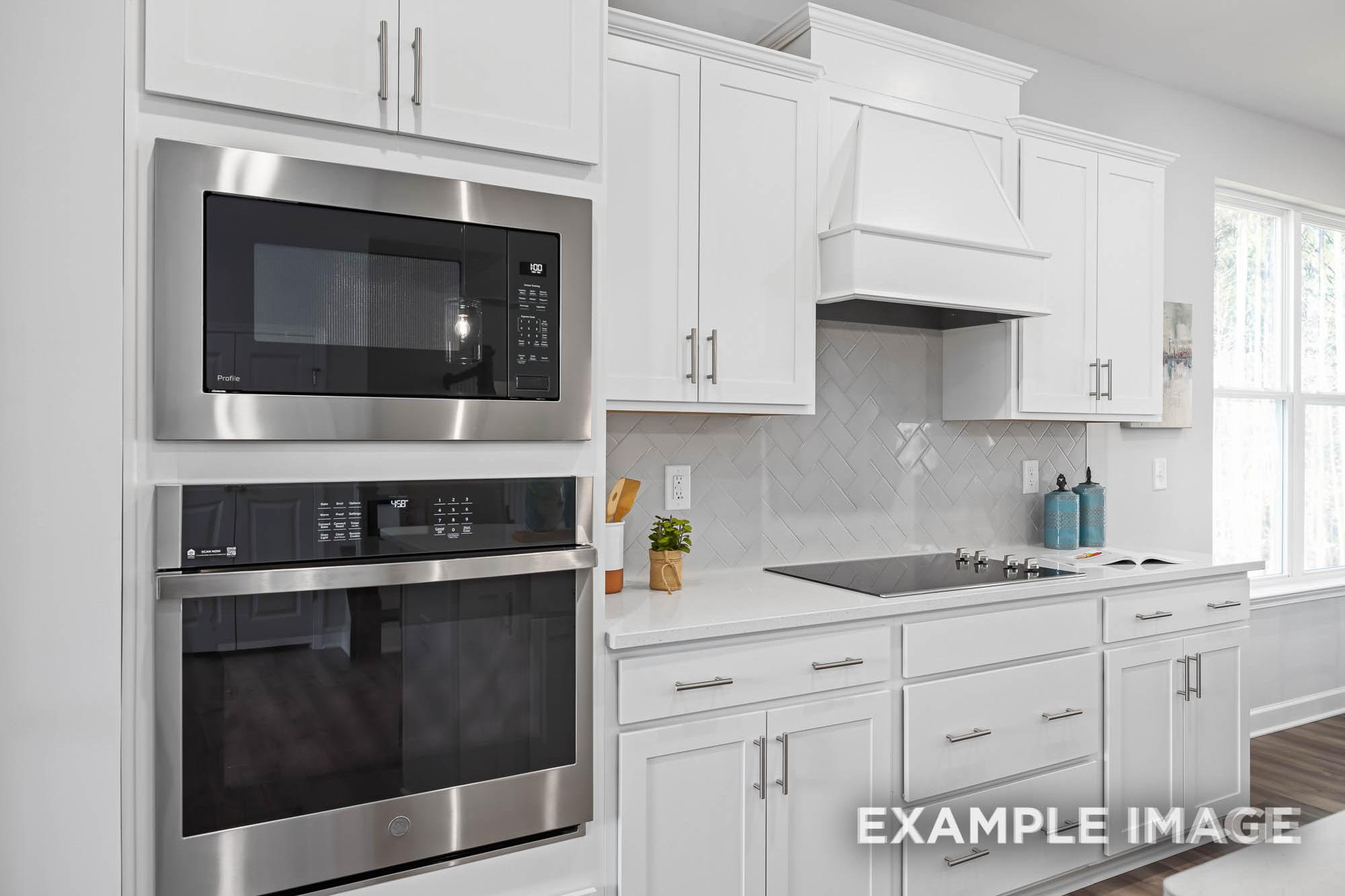 Spacious kitchen in The Ash by Davidson Homes featuring white shaker cabinets, stainless steel double oven, and subway tile backsplash